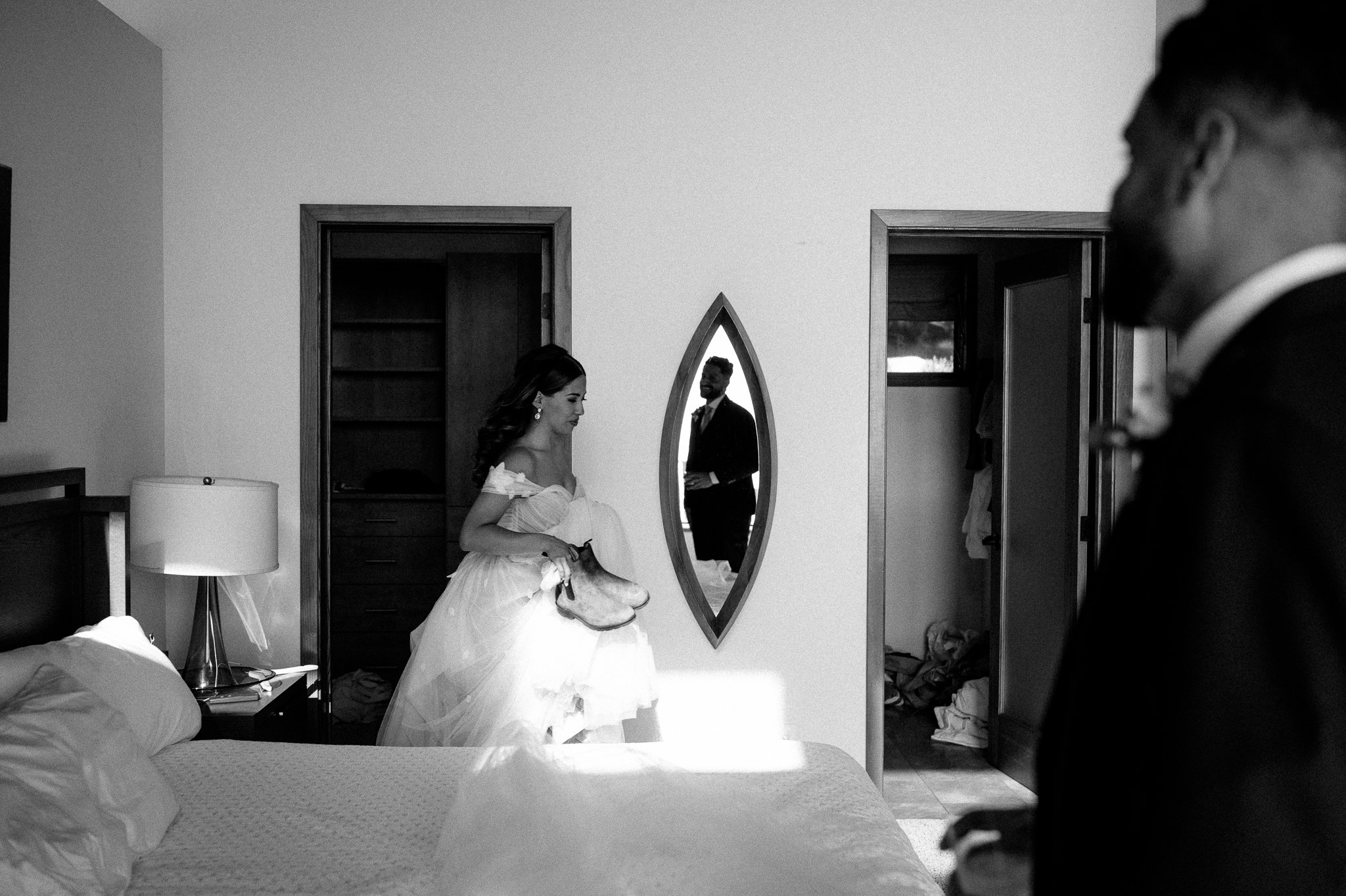 Balck and white photo bride and groom in private room changing shoes with groom's reflection in mirror smiling at bride 