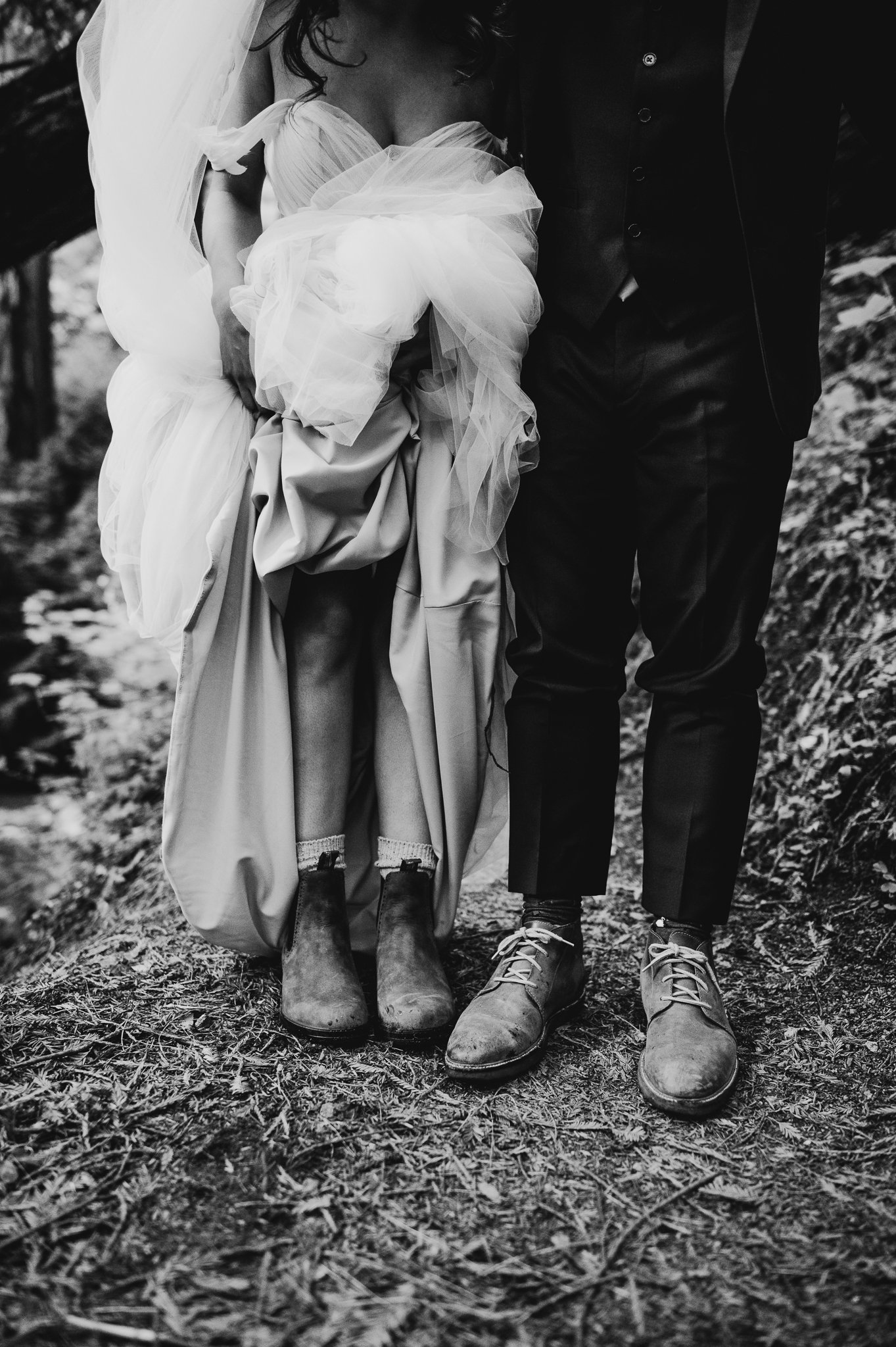 Black and white photo of bride and groom in wedding dress and suit showing hiking shoe 