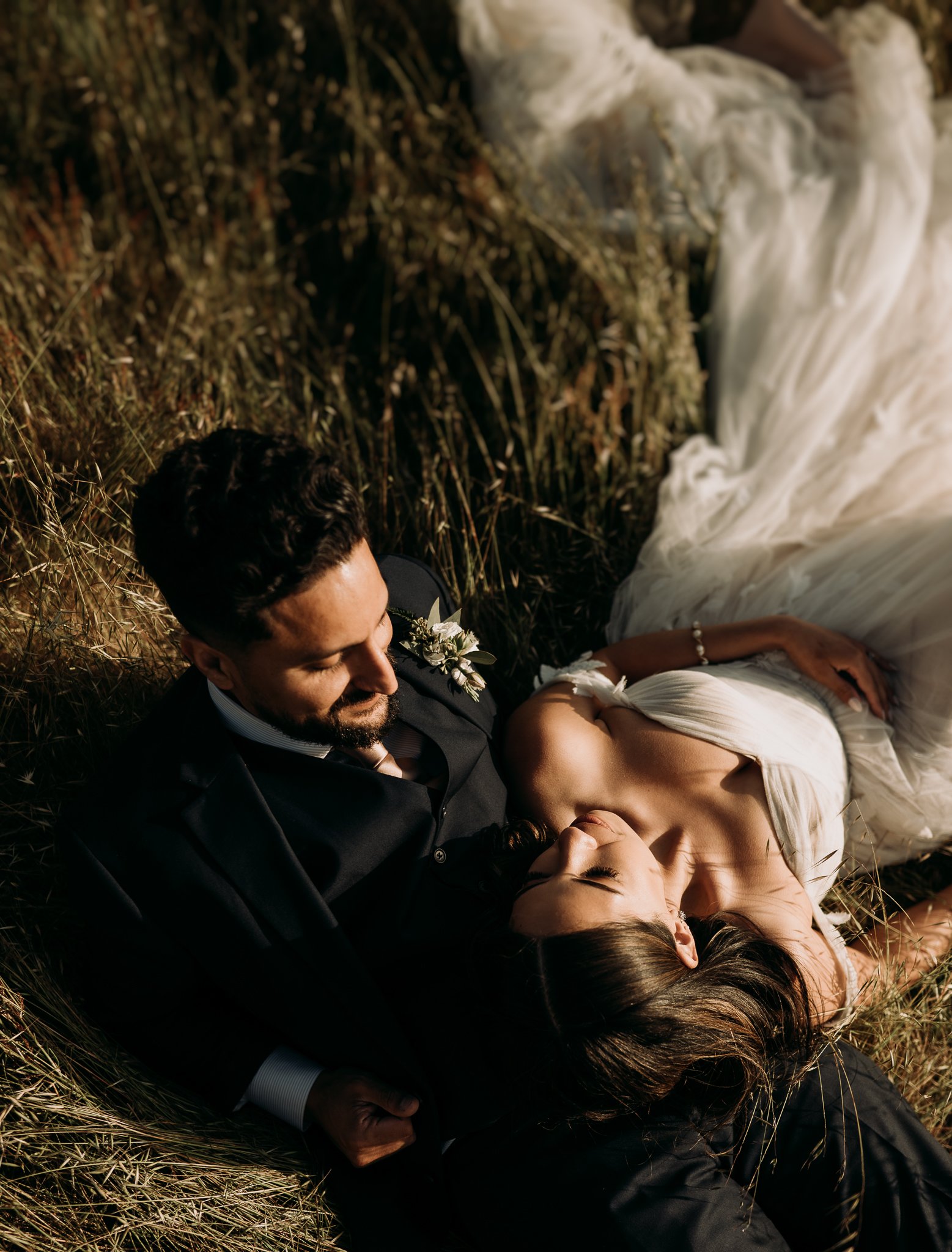 Newly married couple in wedding dress and suit laying in meadow in Big Sur