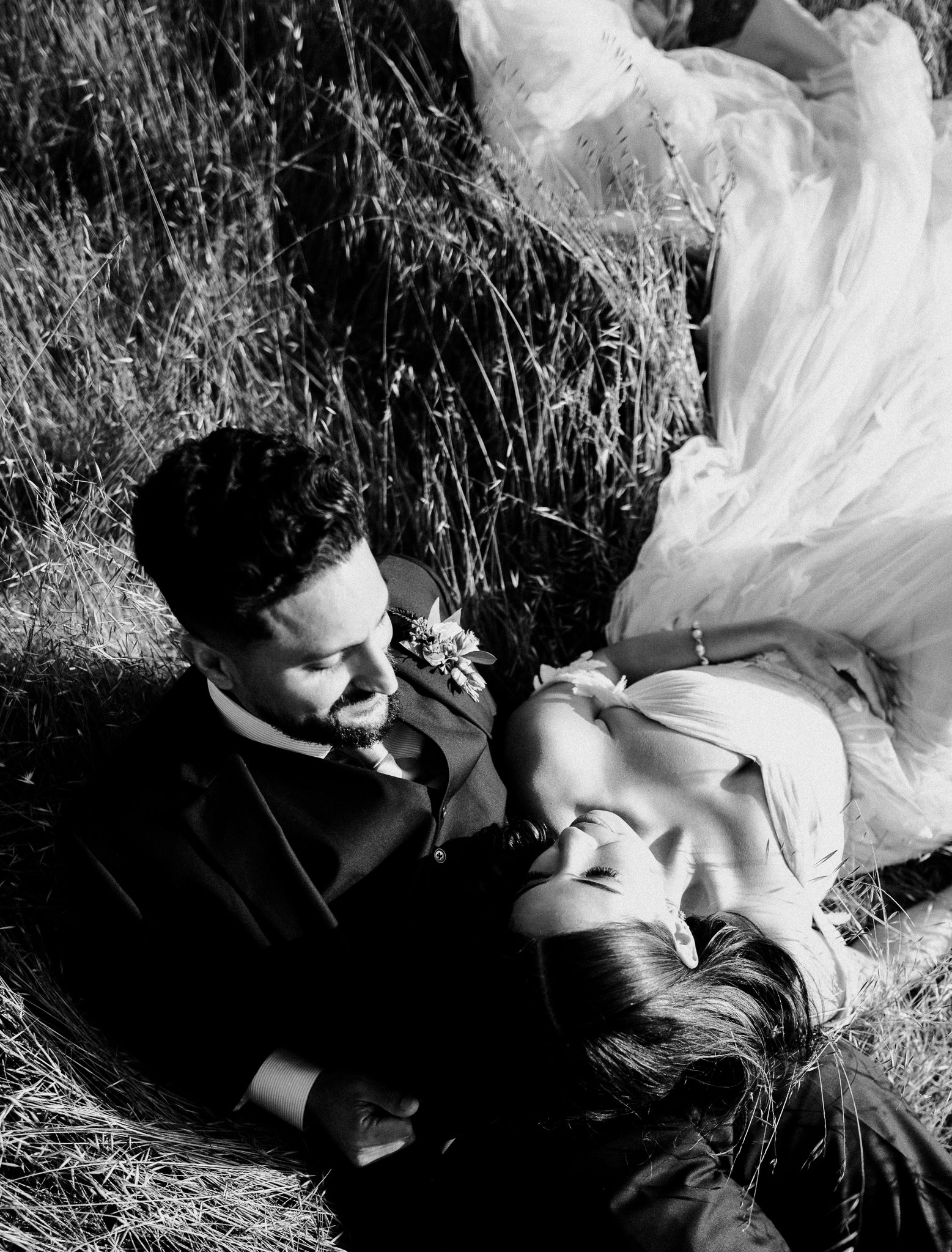 black and white photo newly married couple in wedding dress and suit laying in meadow in Big Sur