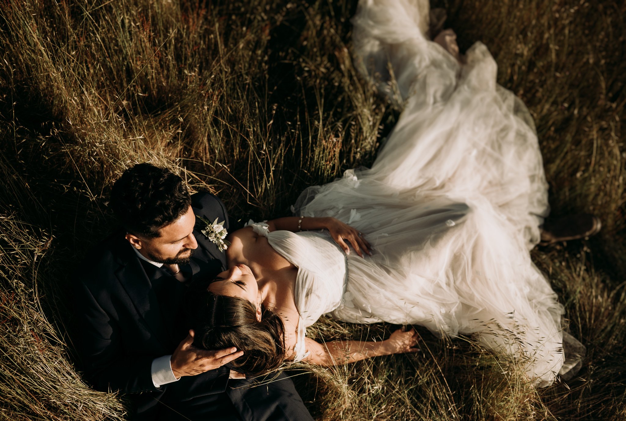 newly married couple in wedding dress and suit laying in meadow in Big Sur