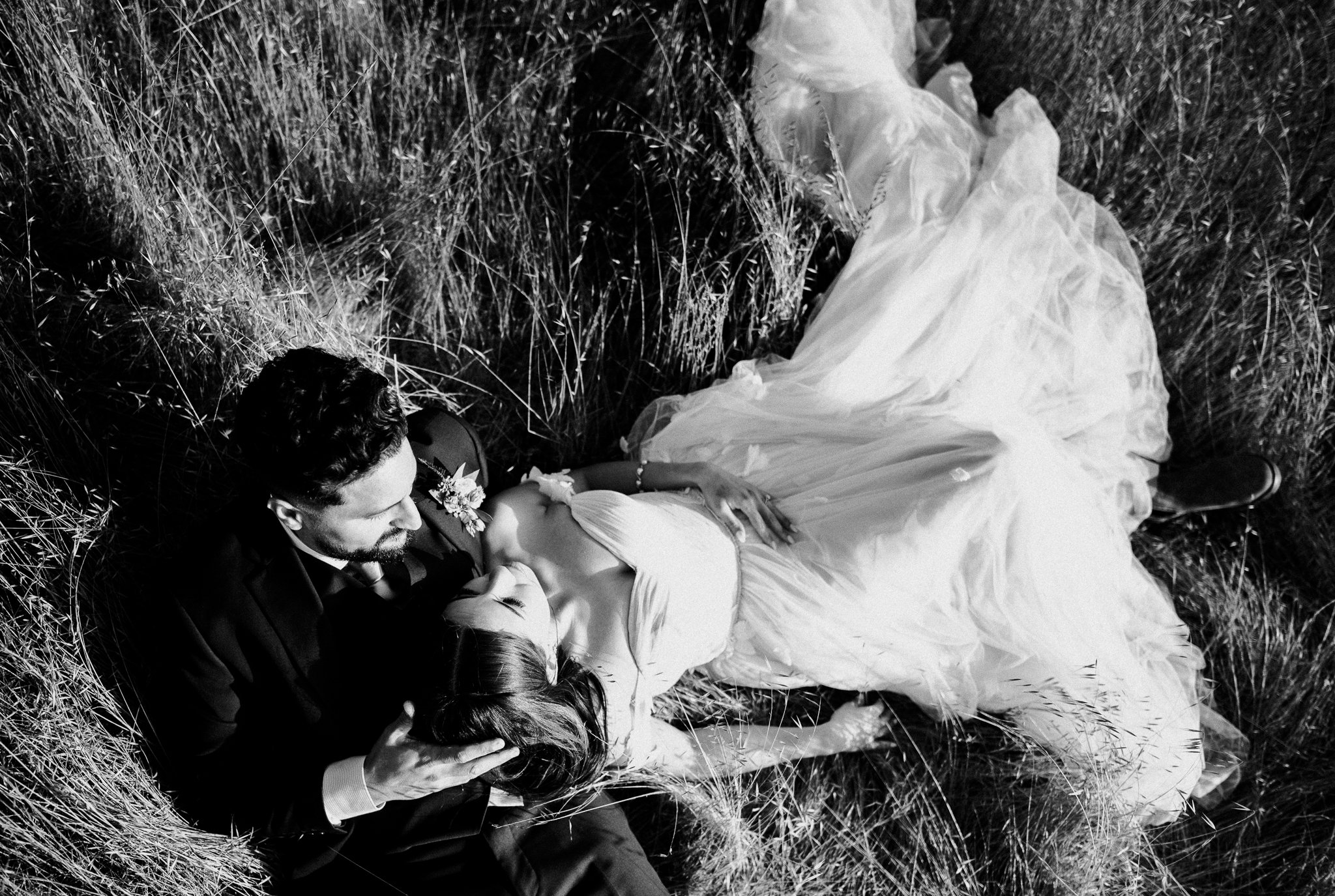 black and white photo newly married couple in wedding dress and suit laying in meadow in Big Sur