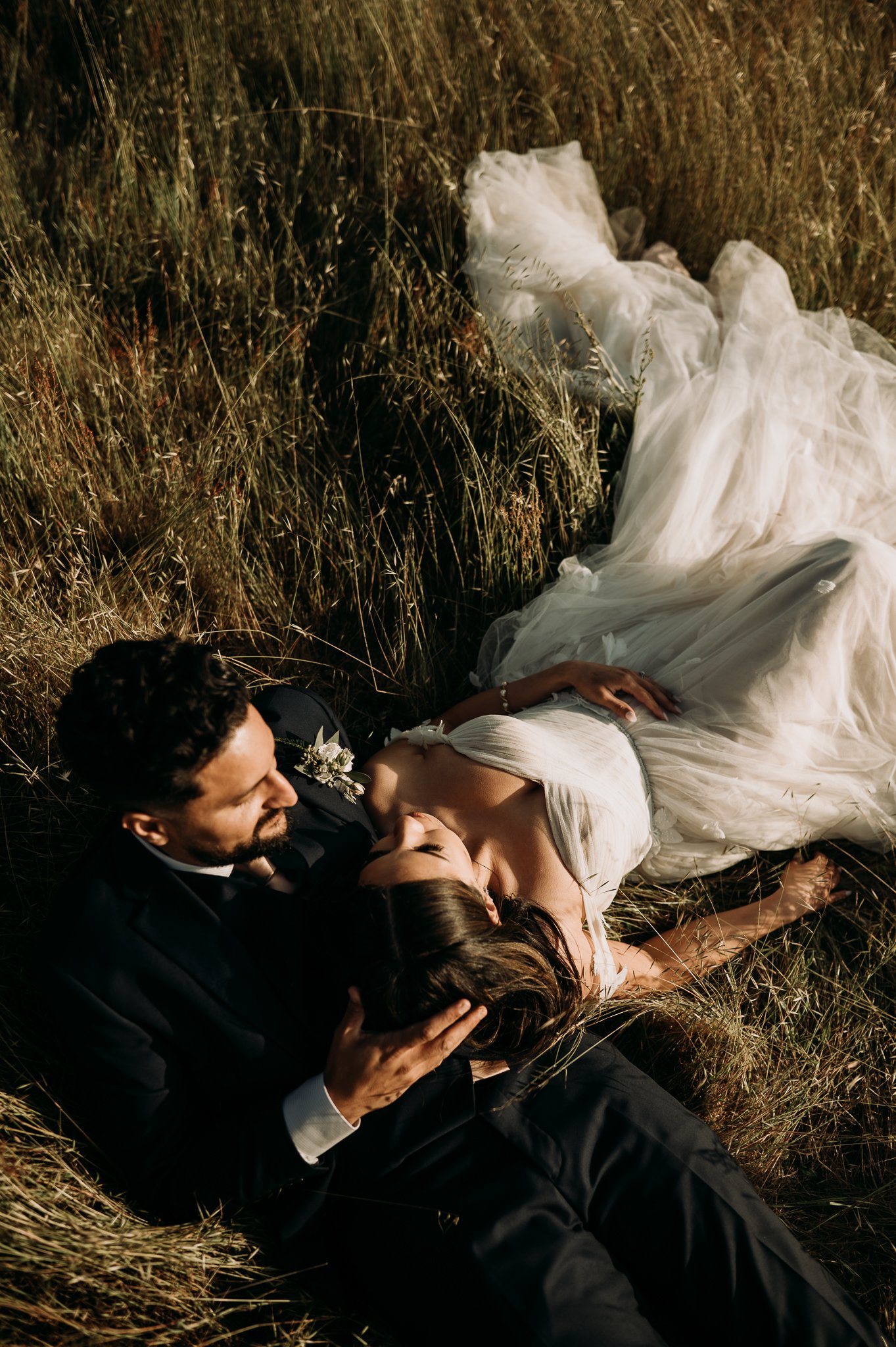  newly married couple in wedding dress and suit laying in meadow in Big Sur