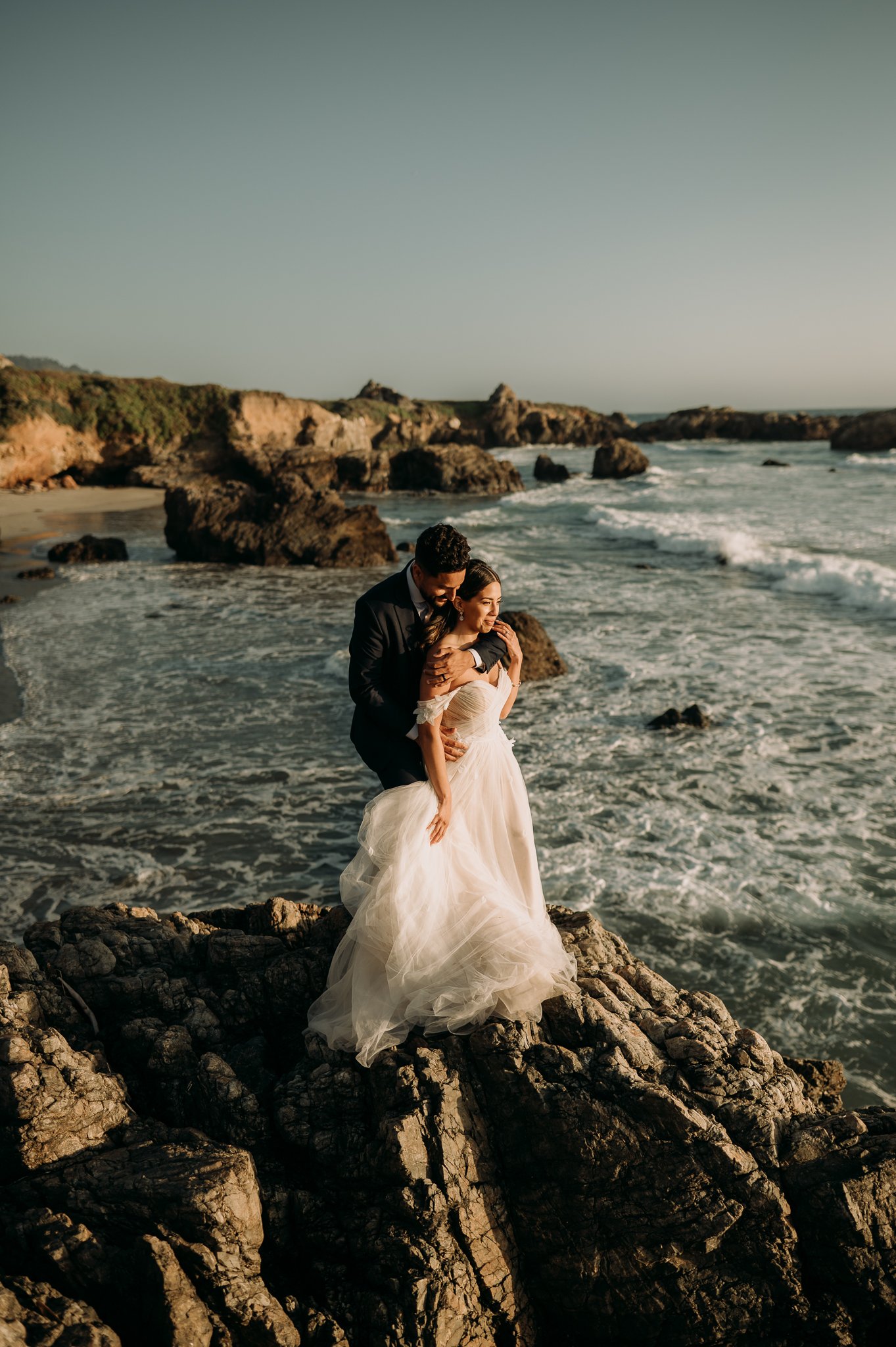 Elopement in Big Sur bride and groom embracing cliffside at sunset 
