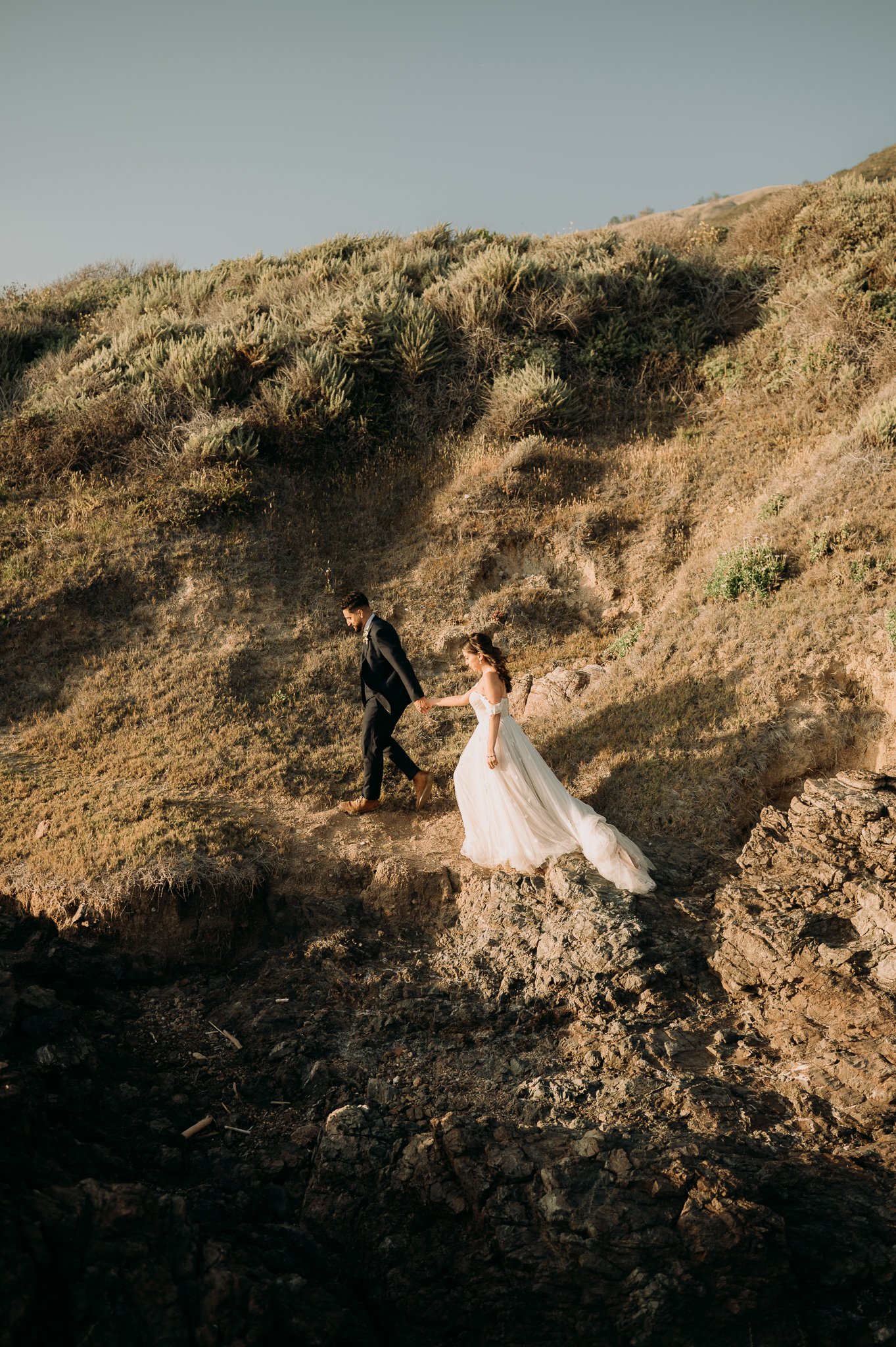 newly married bride and groom walking on cliff in Big Sur California