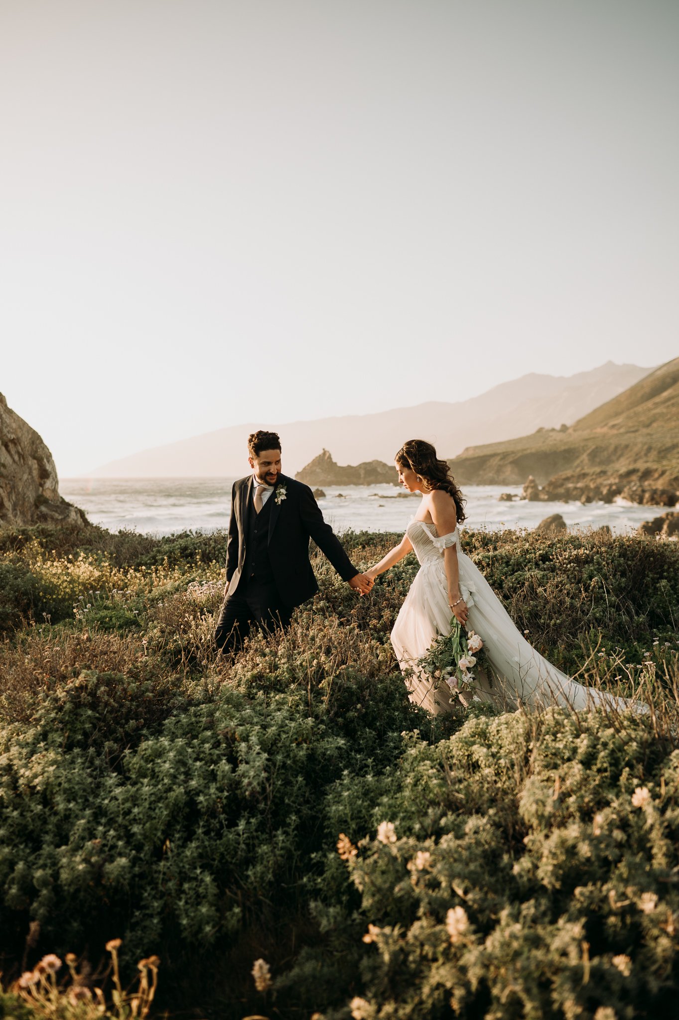 Big Sur Wedding bride and groom in wedding attire walking hand and hand along the Pacific Ocean