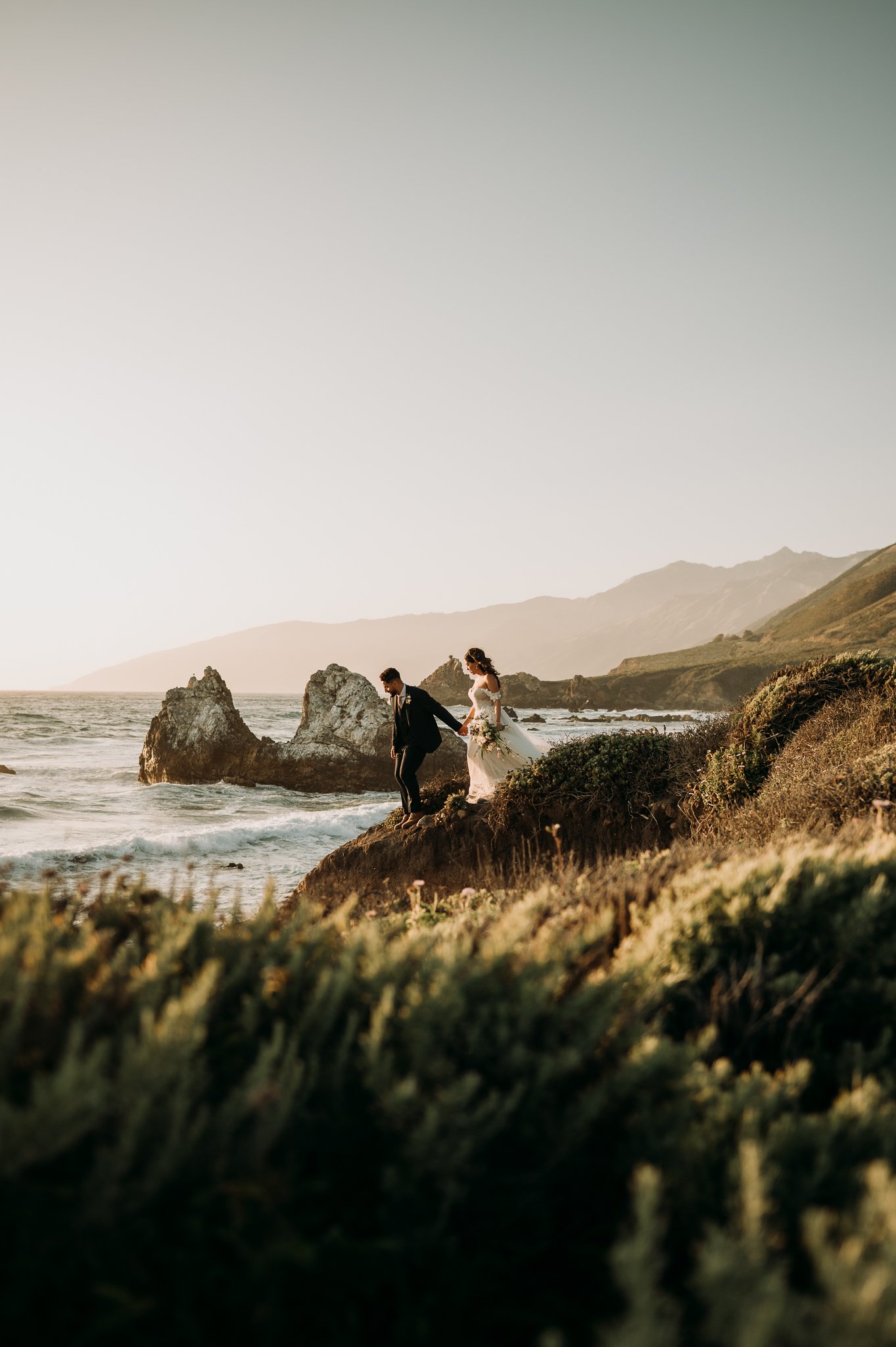 Big Sur Wedding bride and groom in wedding attire walking hand and hand down toward Pacific Ocean