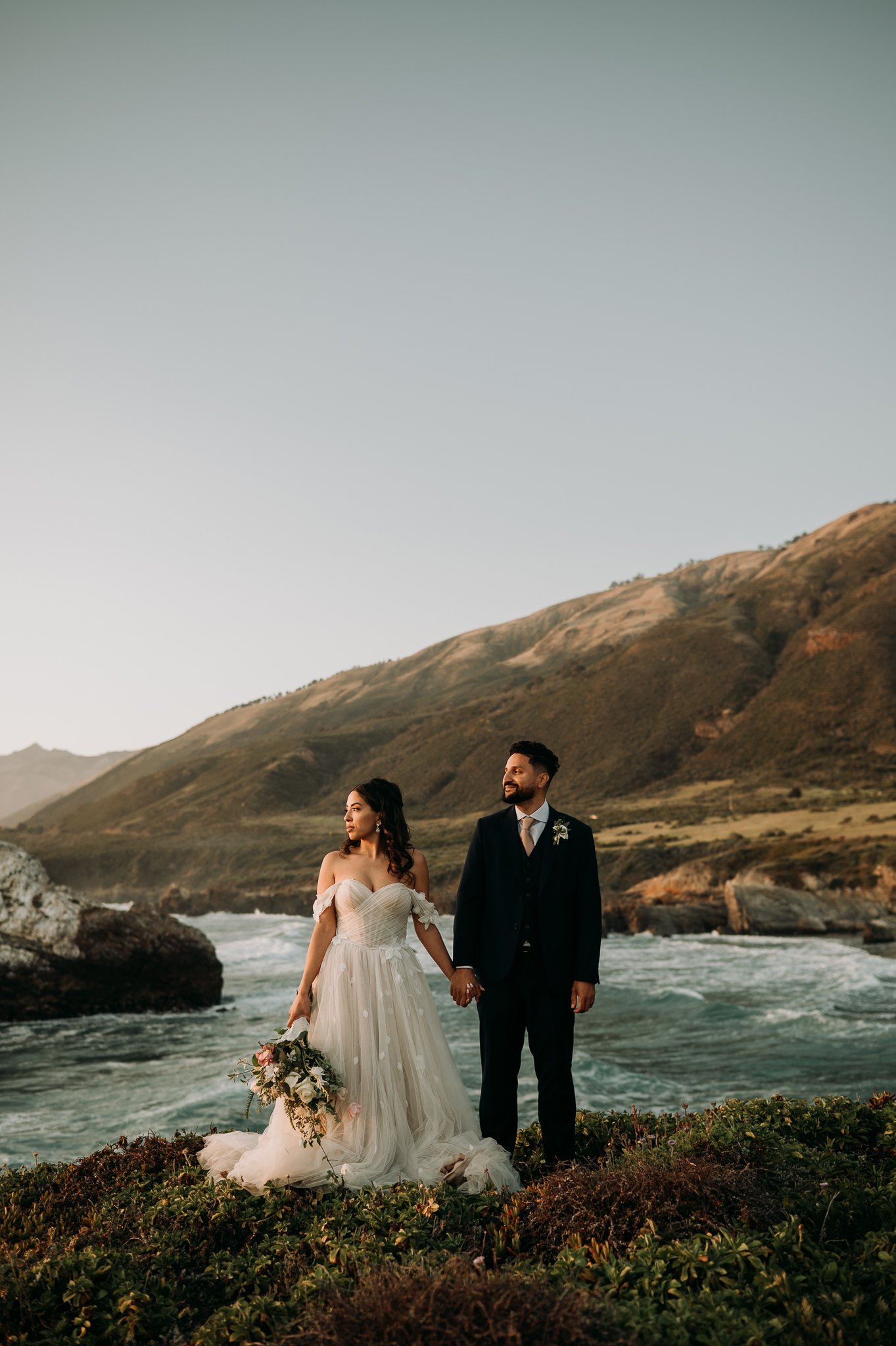 bride and groom standing side by side looking out at the Pacific Ocean