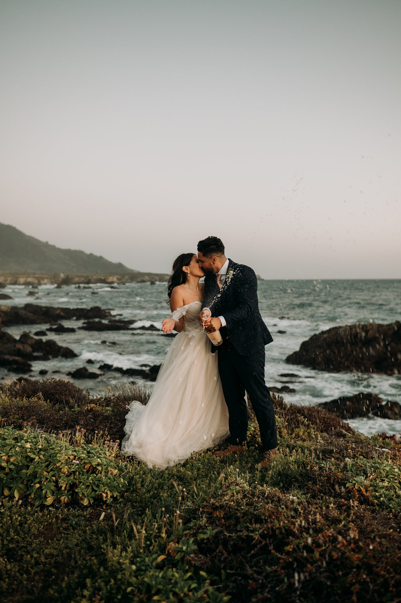 bride and groom opening champagne cliffside in Big Sur