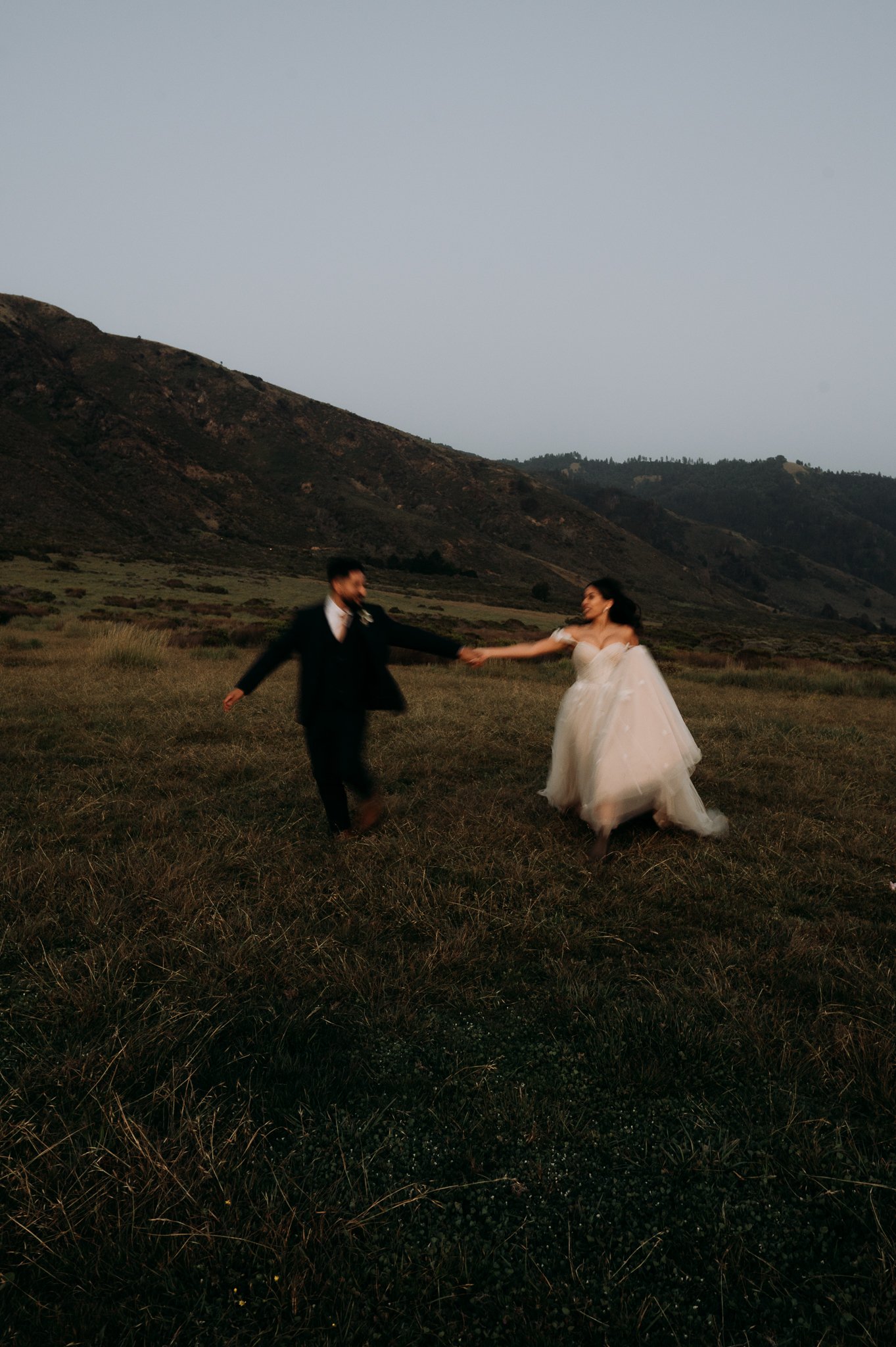 bride and groom running hand and hand in meadow in Big Sur