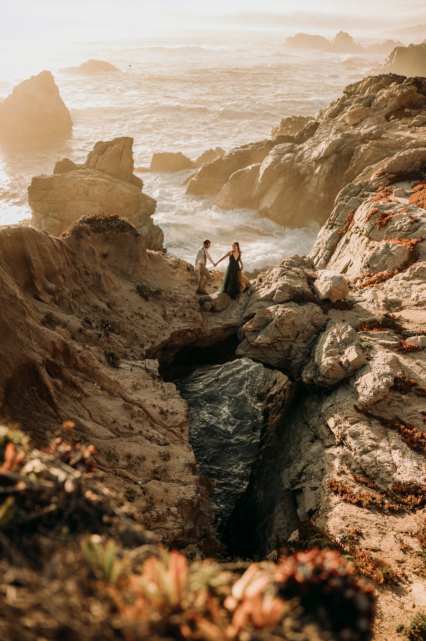Newly engaged couple at Big Sur, California on cliffs with Pacific Ocean waves behind them