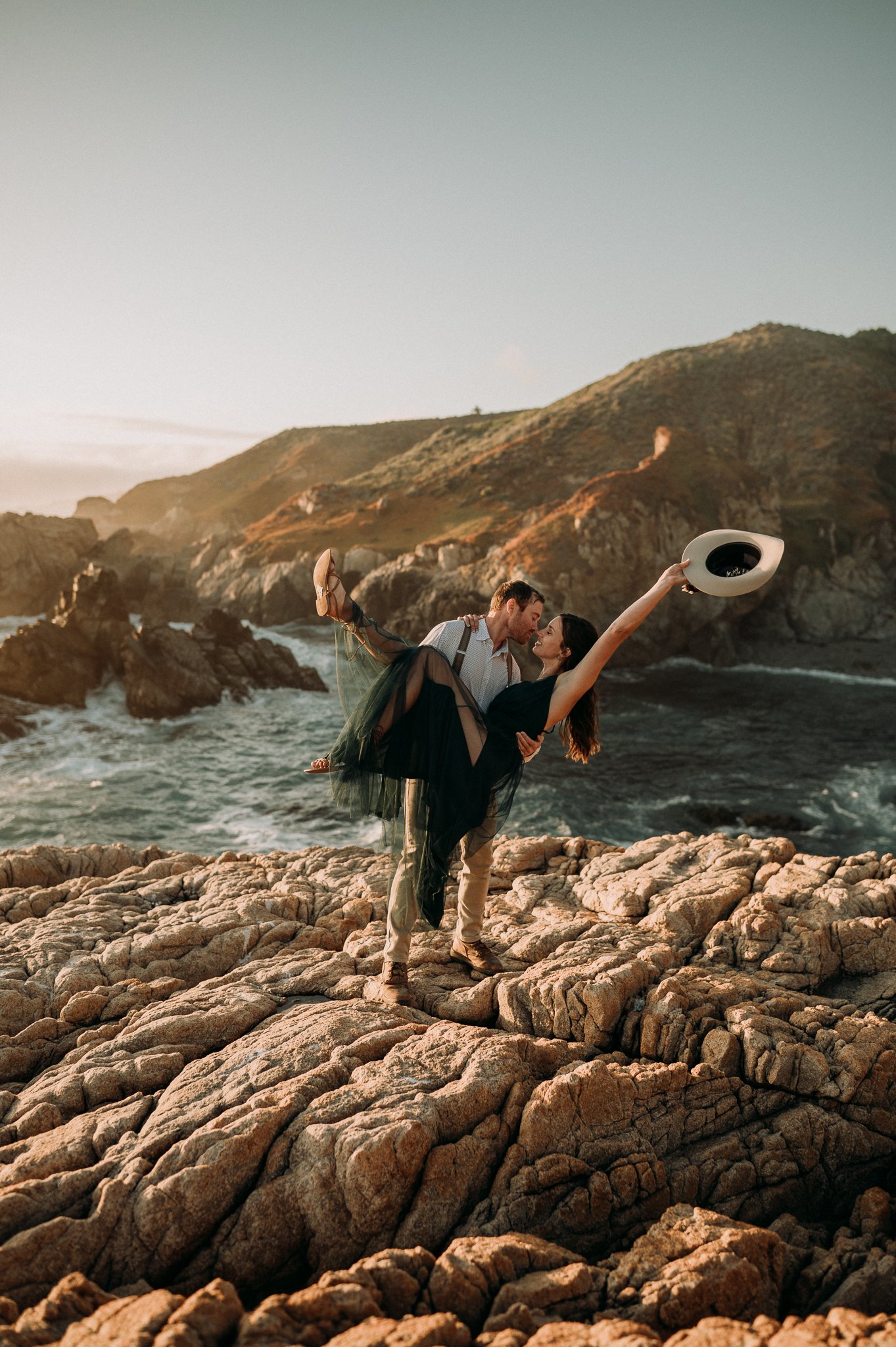 Couple posing on cliff in Big Sur California he is holding her and kissing