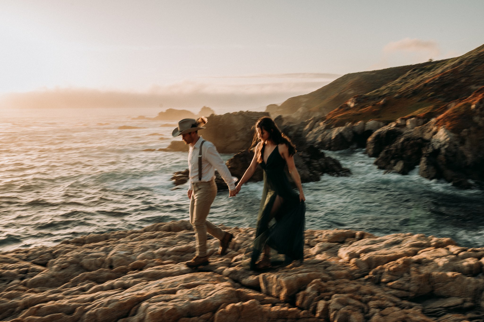 Newly engaged couple walking on cliff with Pacific ocean in background 