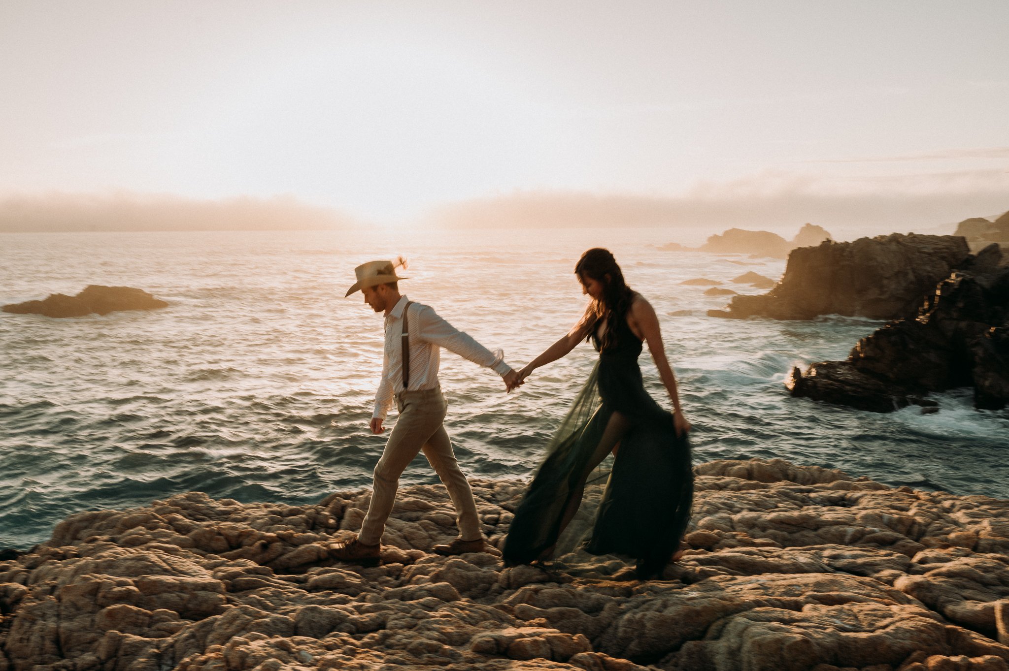 Newly engaged couple posing on cliff with Pacific ocean and beautiful sunset in background 