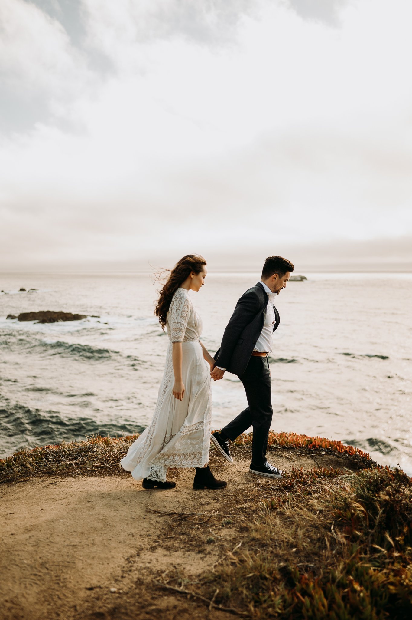 Newly engage couple walking on cliffs hand in hand in Big Sur