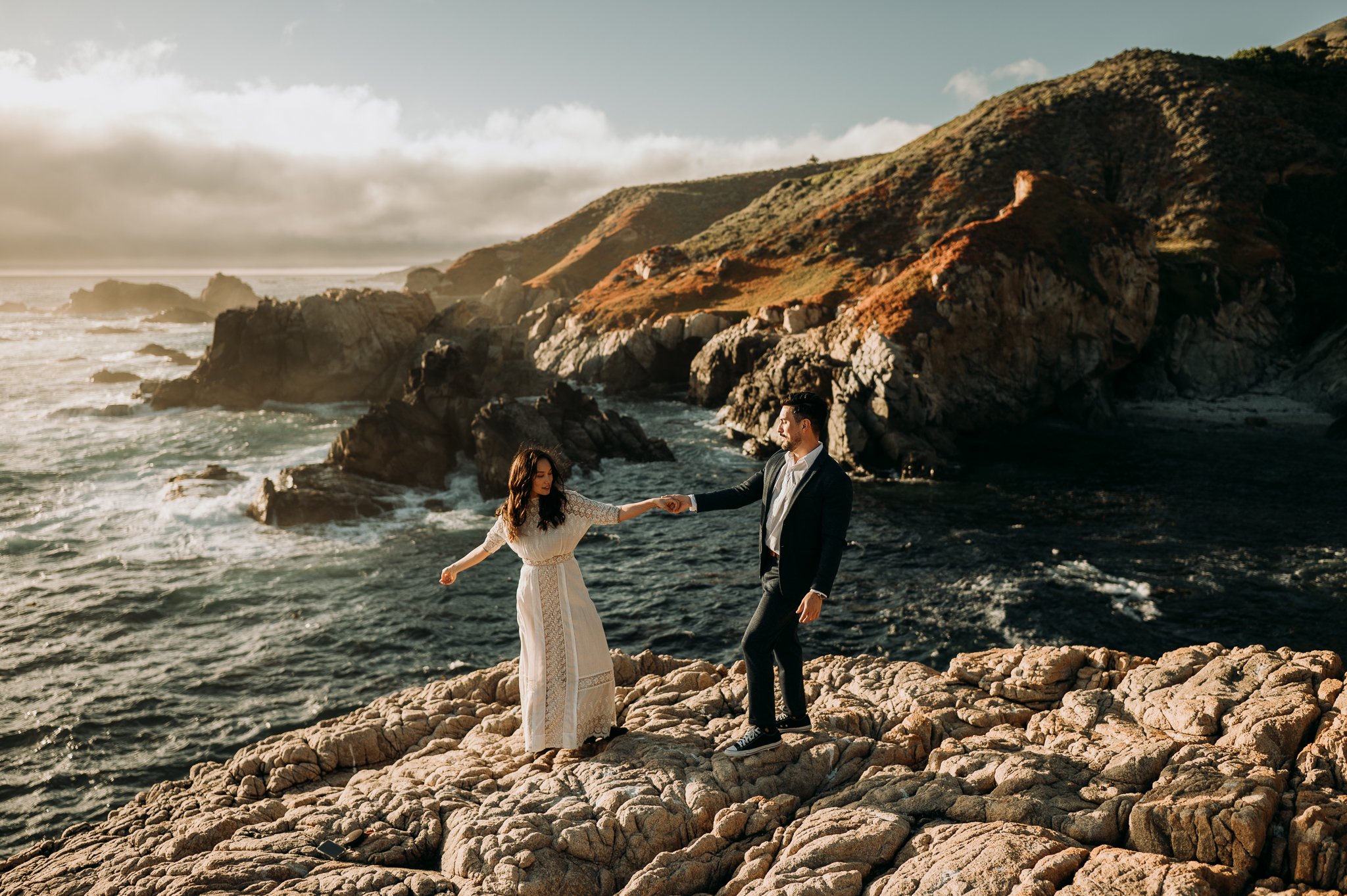 Newly engaged couple dancing on cliff with Pacific Ocean in background