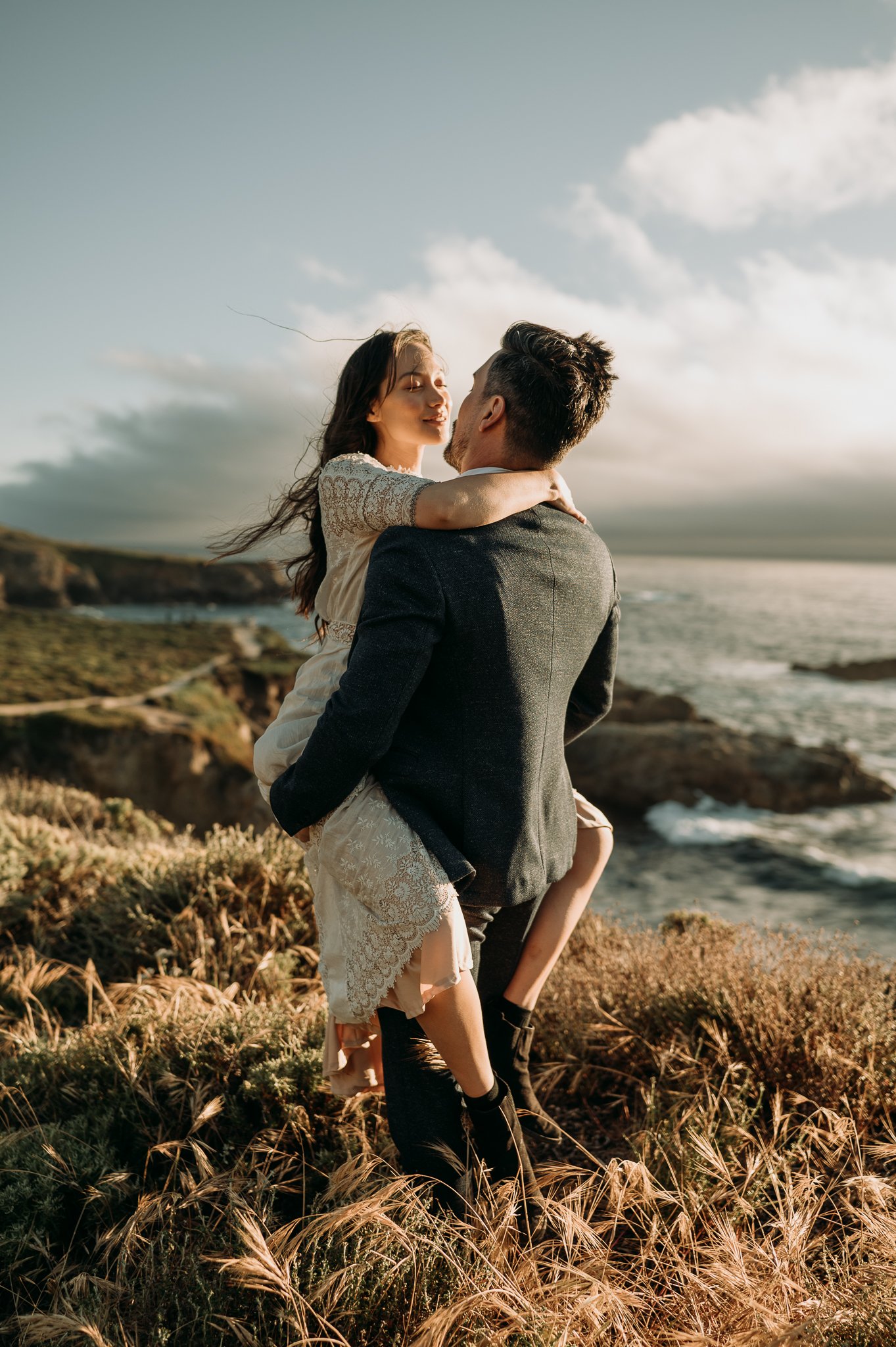  couple kissing with woman's legs around man's waist with Pacific Ocean in background
