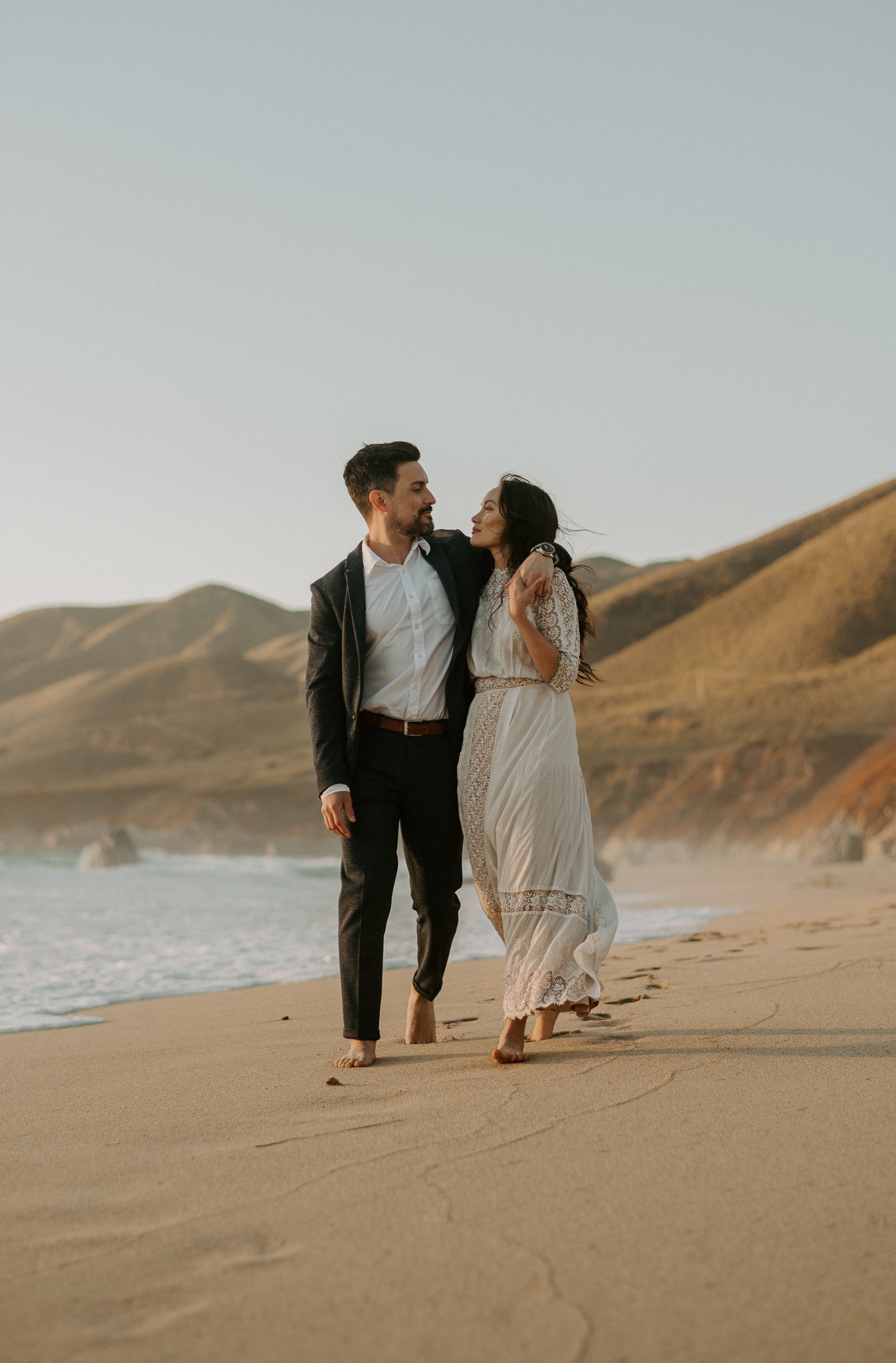 Newly engaged couple walking on beach looking at each other Big Sur