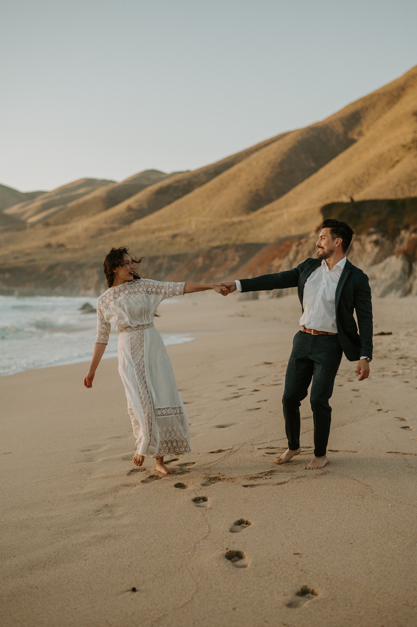 Newly engaged couple walking on beach holding hands Big Sur
