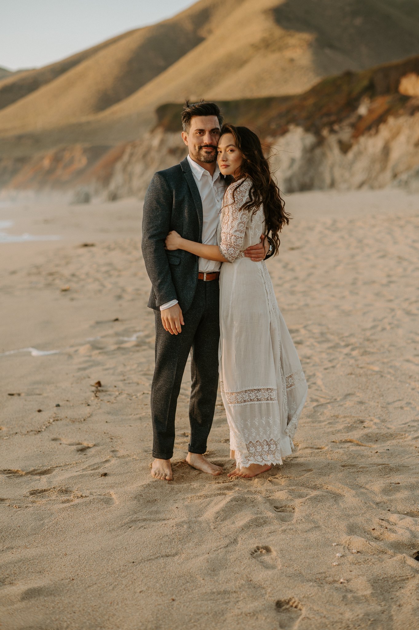 Newly engaged couple hugging looking at camera on beach Big Sur
