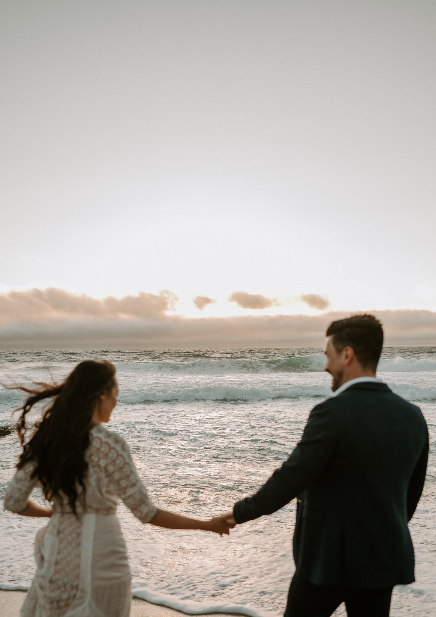 engagement couple holding hands walking in water on beach in Big Sur