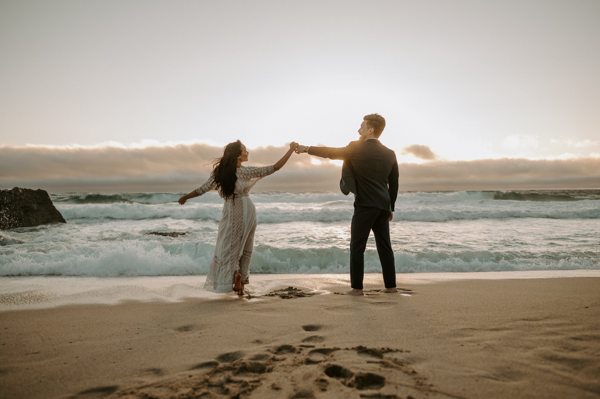 engagement couple holding hands walking in water on beach in Big Sur