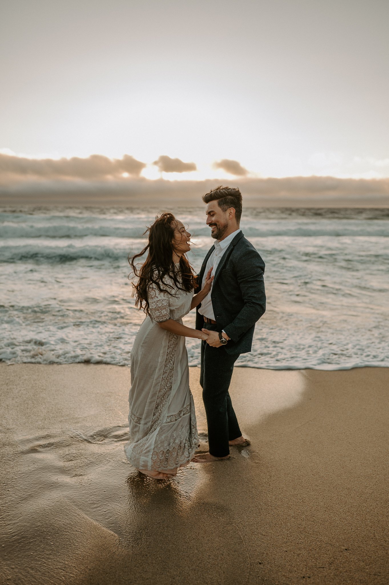 engagement couple at sunset dancing in water on beach in Big Sur