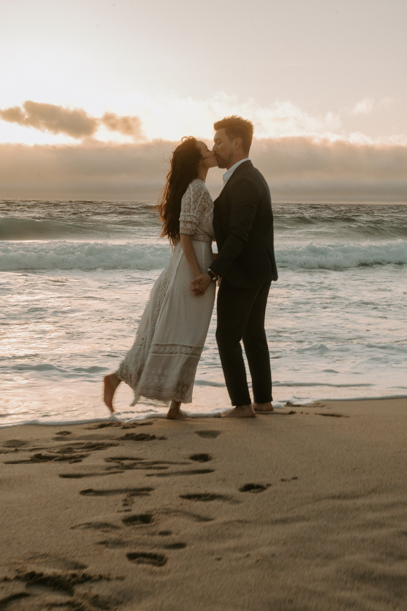 engagement couple at sunset kissing in water on beach in Big Sur