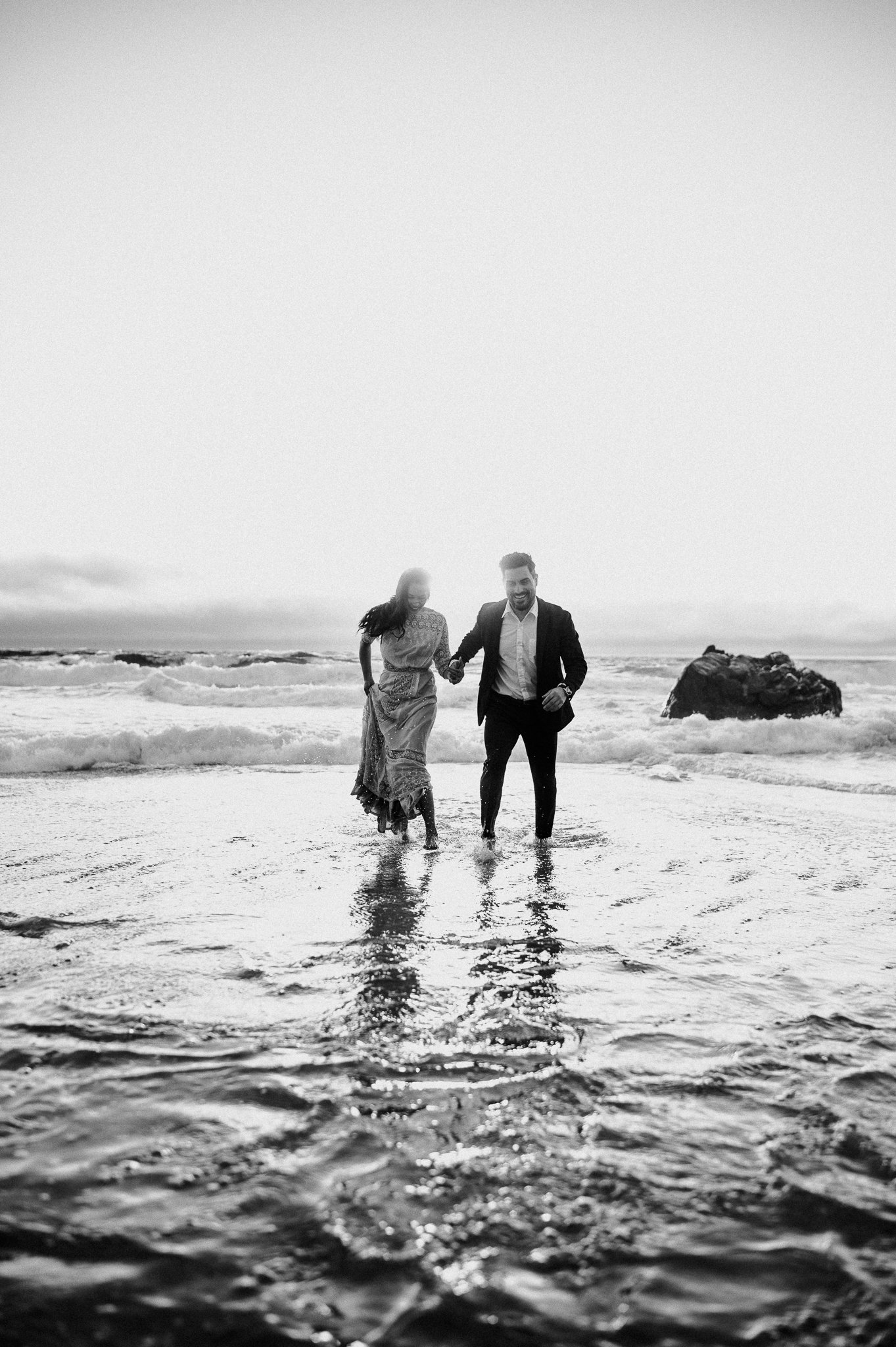 engagement couple running in ocean along in shoreline in Big Sur