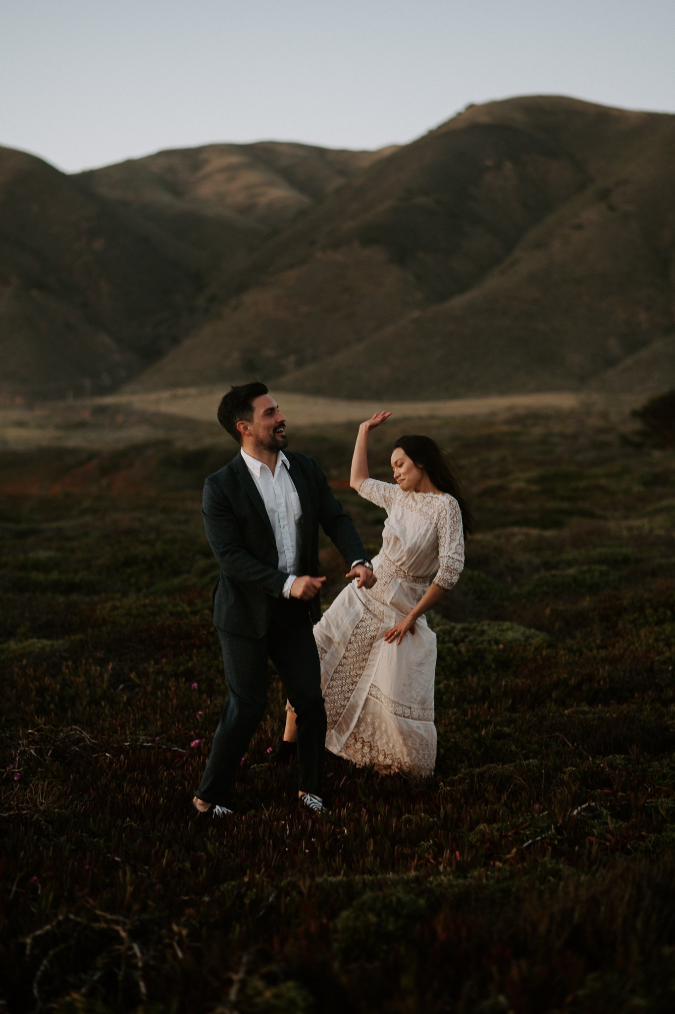 Engaged couple dancing in meadow in Big Sur with hills in background