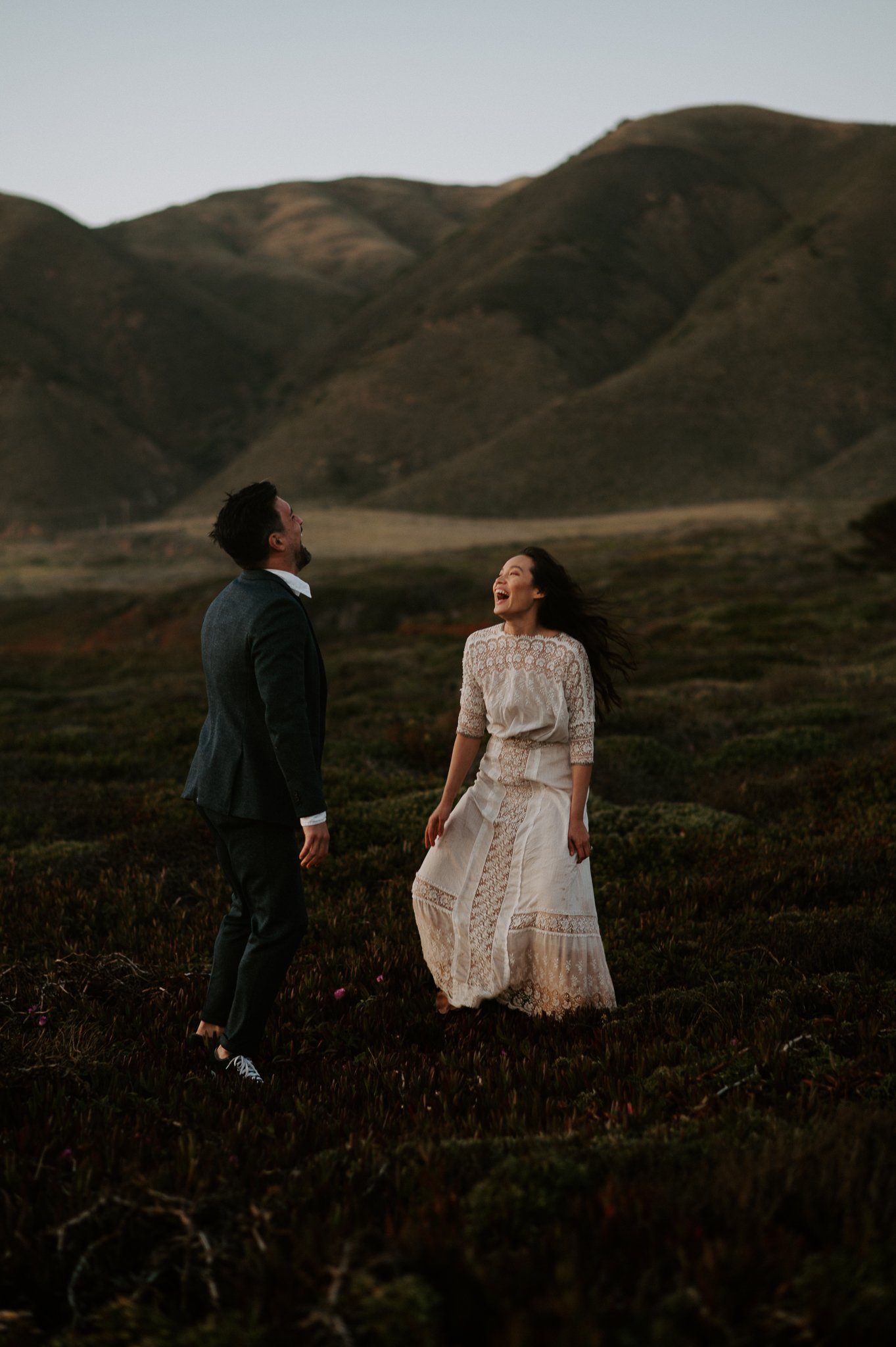 Engaged couple dancing in meadow in Big Sur with hills in background