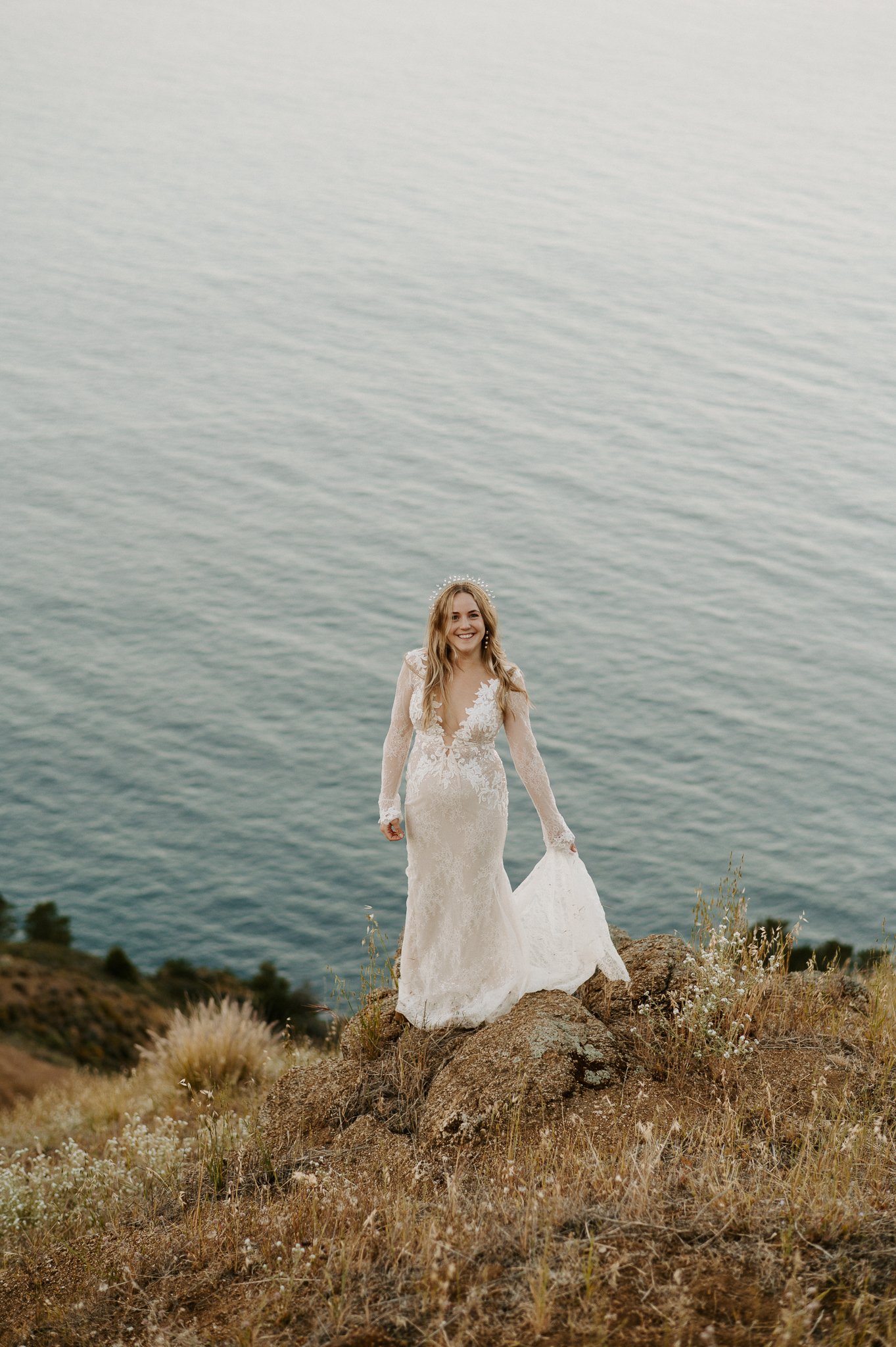 Bride in wedding dress standing on edge cliff with Pacific Ocean behind her