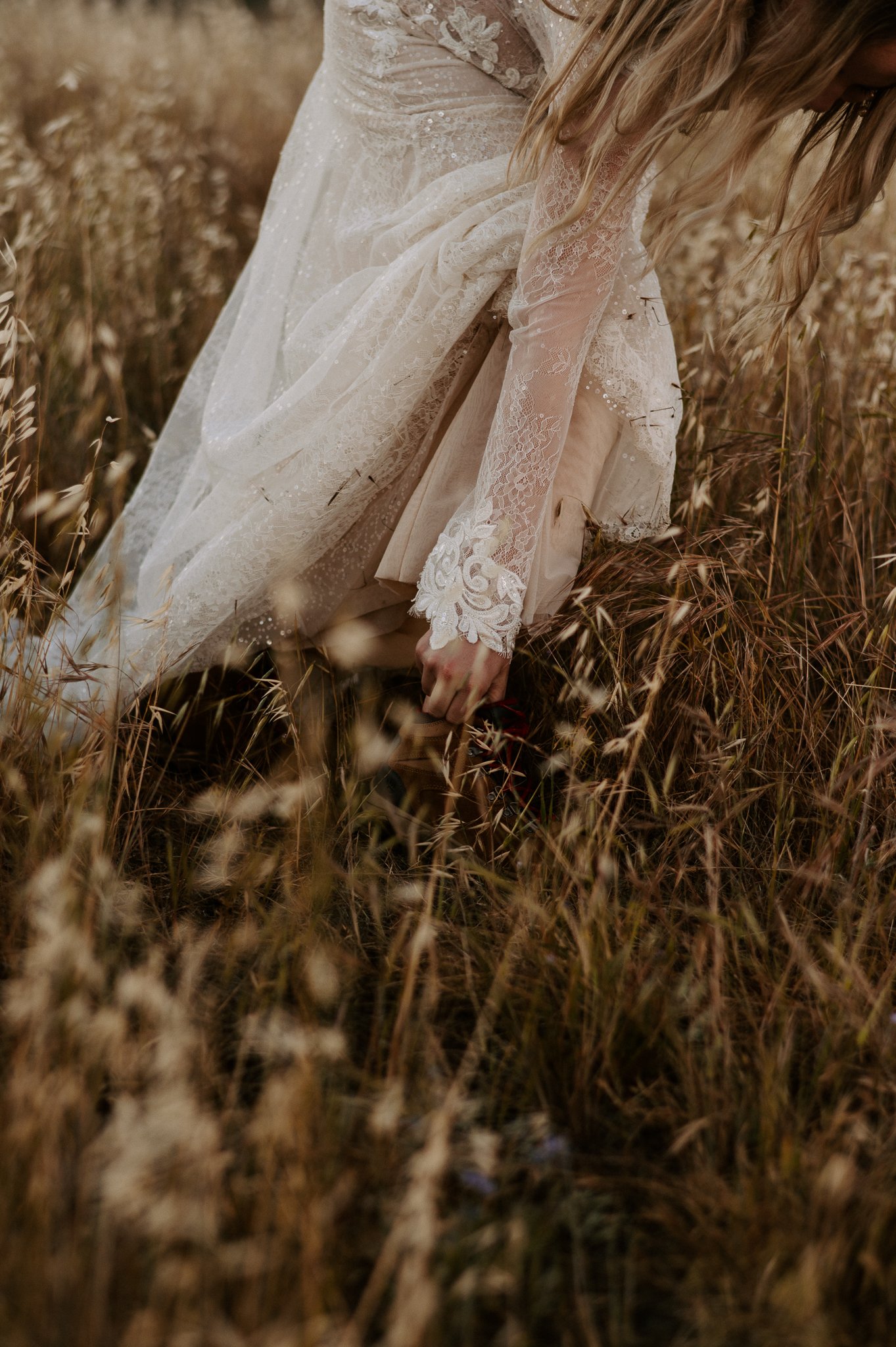 Bridal veil in tall brown grass of Big Sur, bride is adjusting her hiking book
