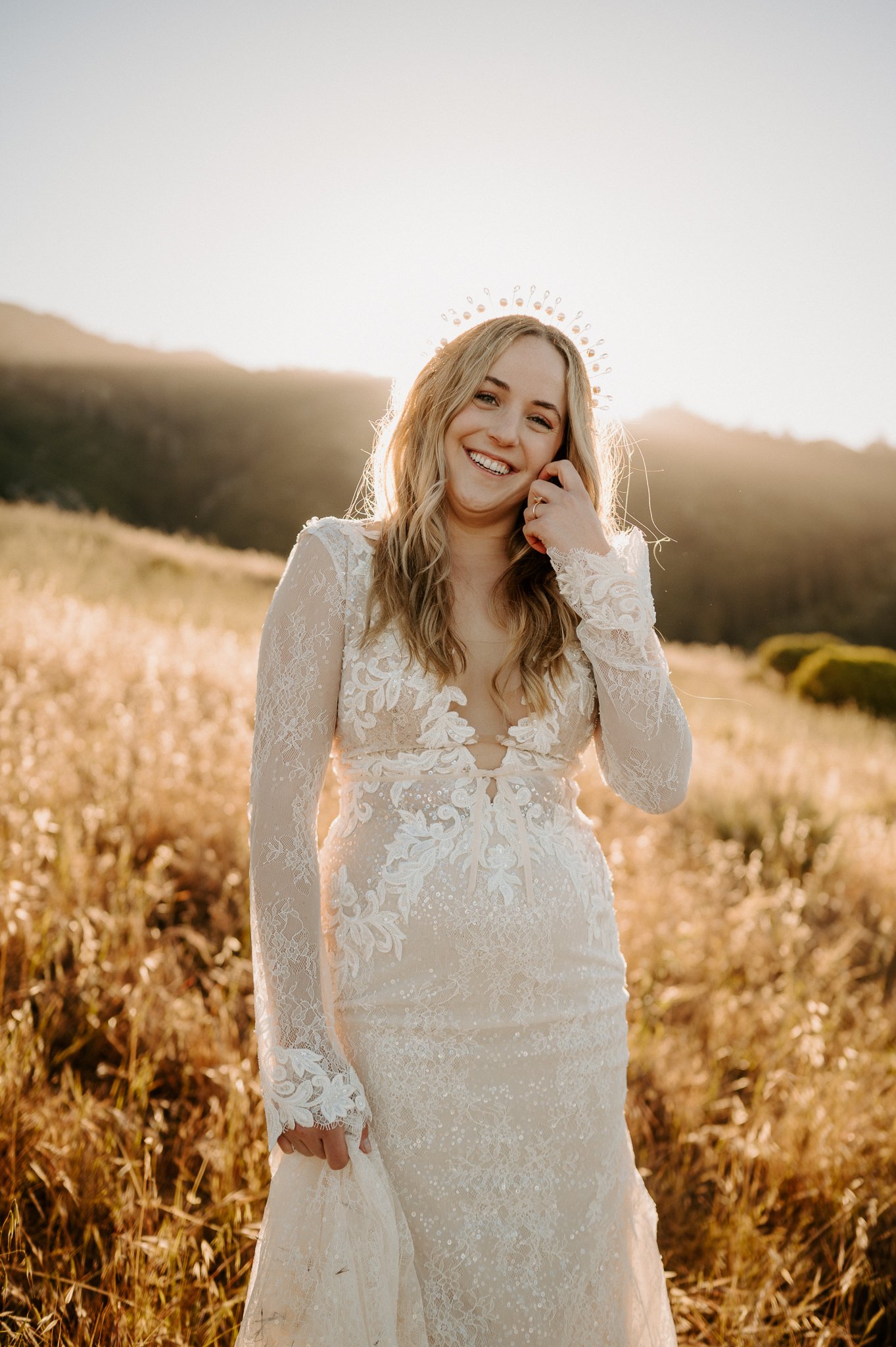Big Sur Bride posing in tall grass, in lace wedding dress she is smiling