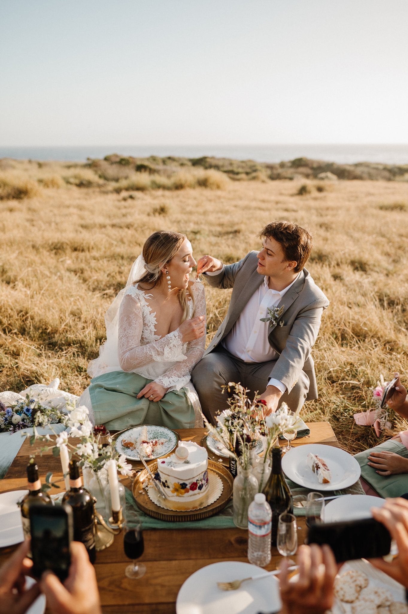 Big Sur Wedding cliffside picnic with groom feeding bride wedding cake