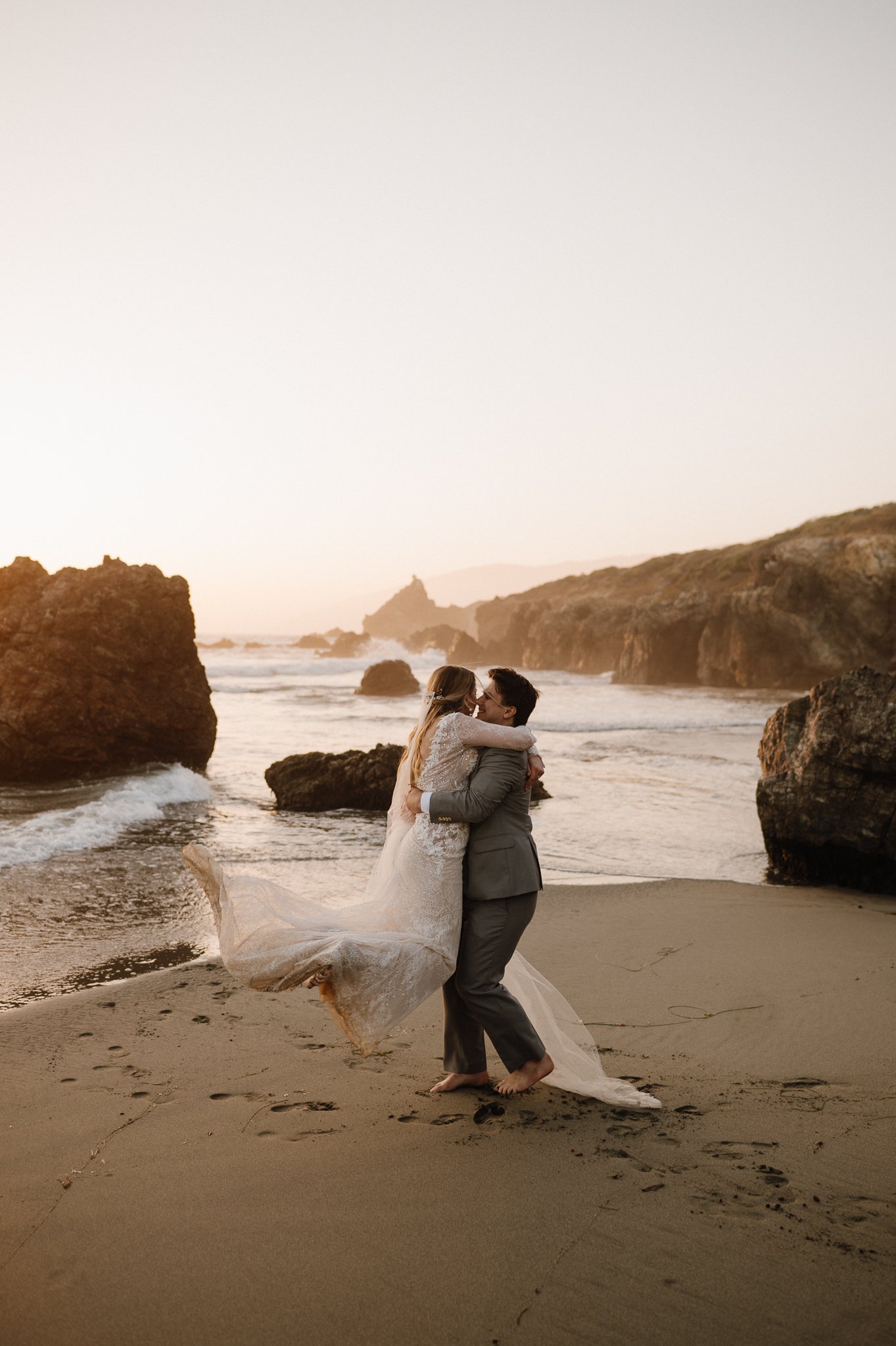 Big Sur bride and groom on beach, groom in lifting bride off the ground spinning her around