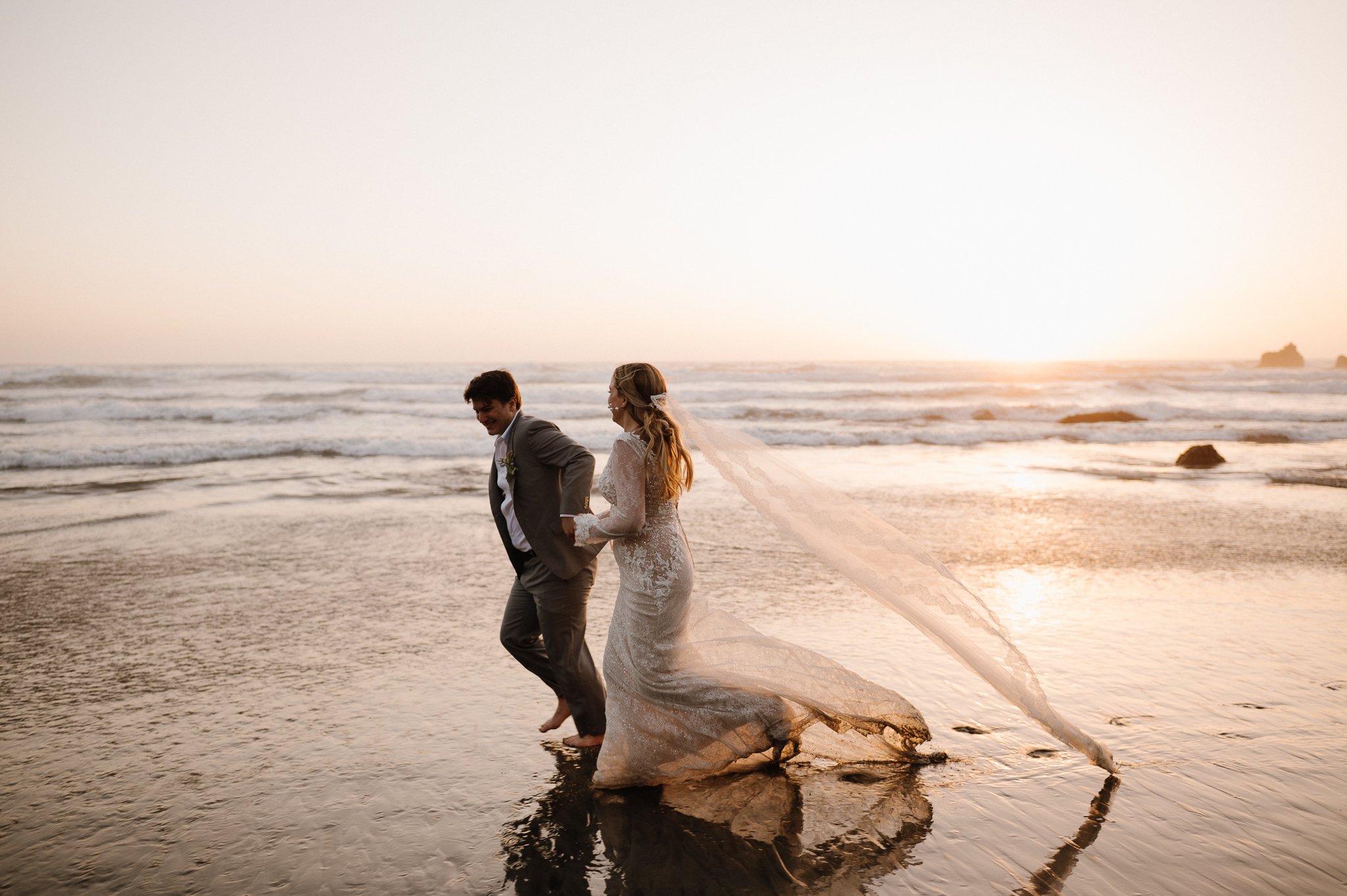 Big Sur bride and groom running through ocean water on beach holding hands 