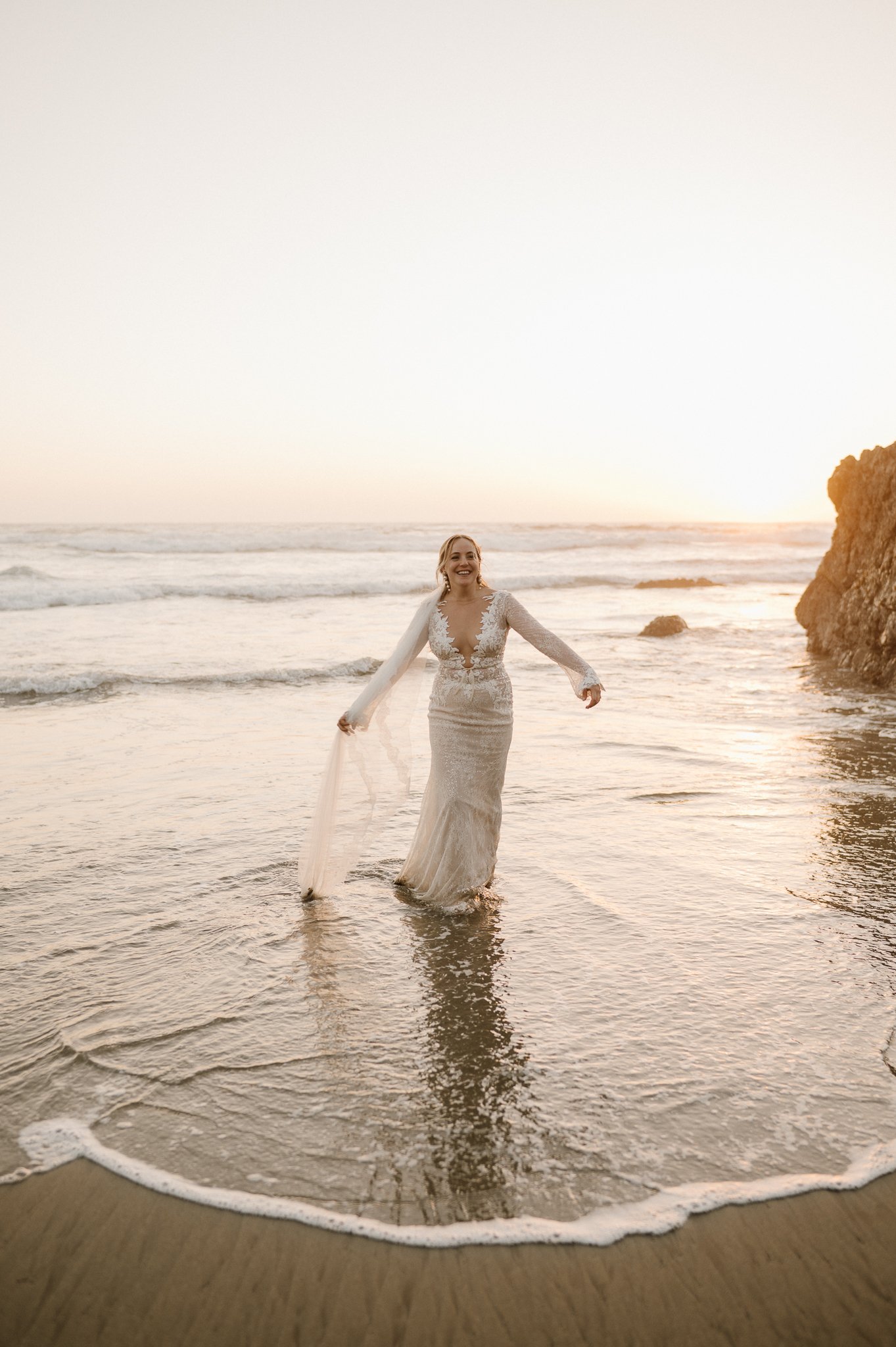 Big Sur Wedding bride standing in ocean water holding her wet dress out to the side