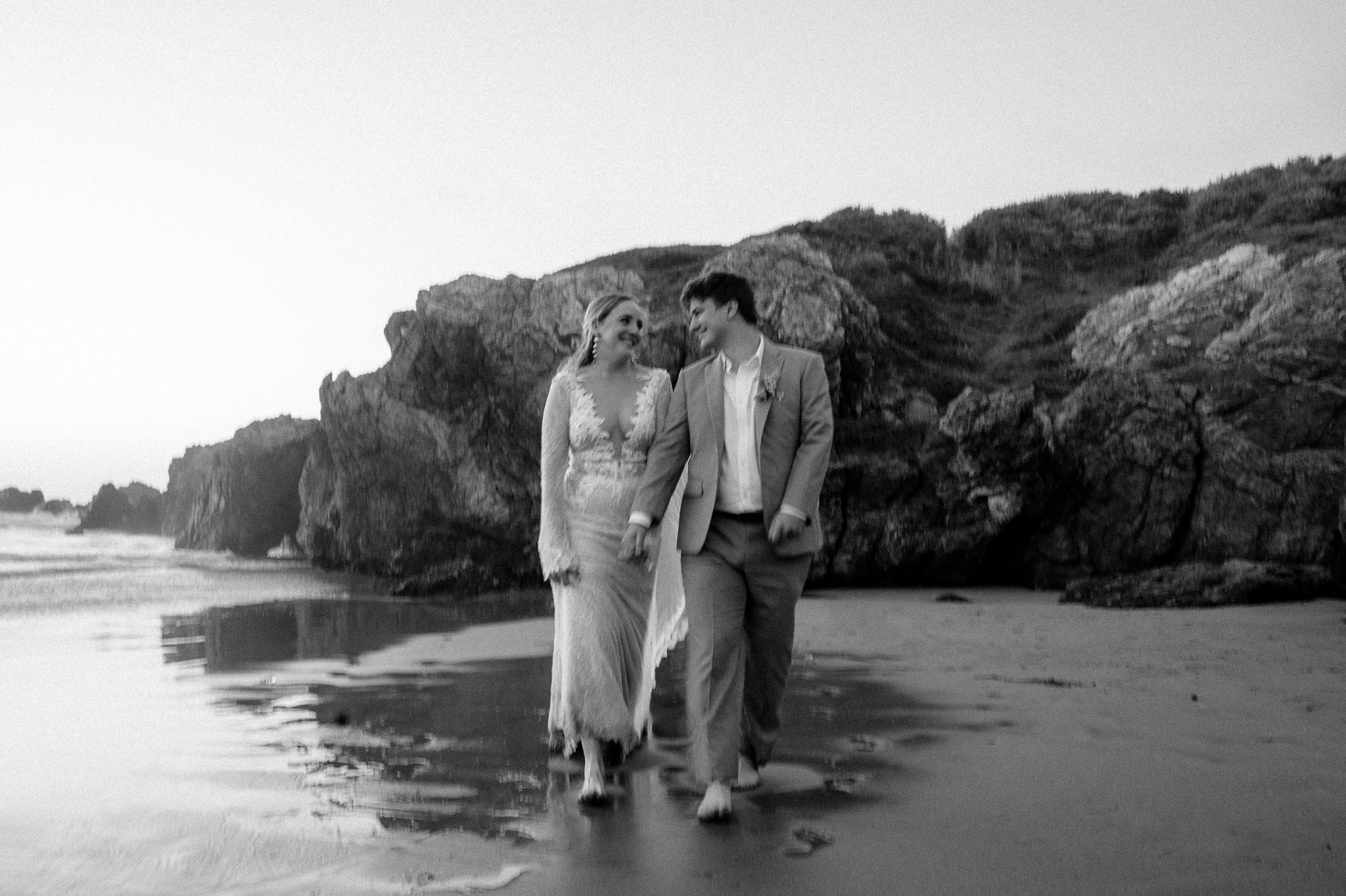 black and white of bride and groom walking on beach hand in hand