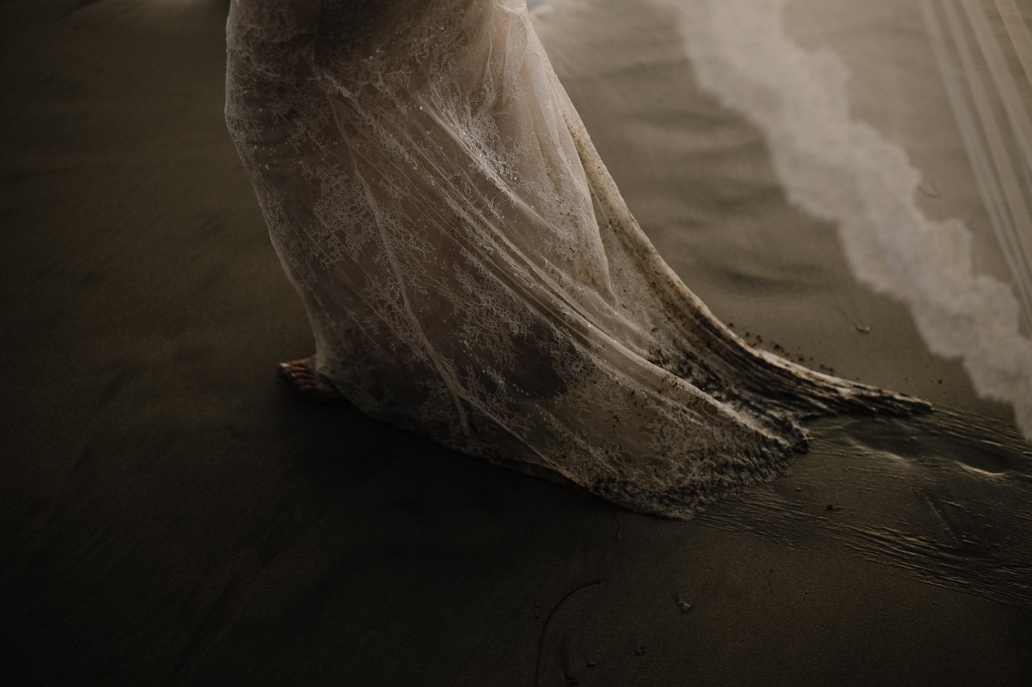 bottom of brides lace wedding dress in beach sand