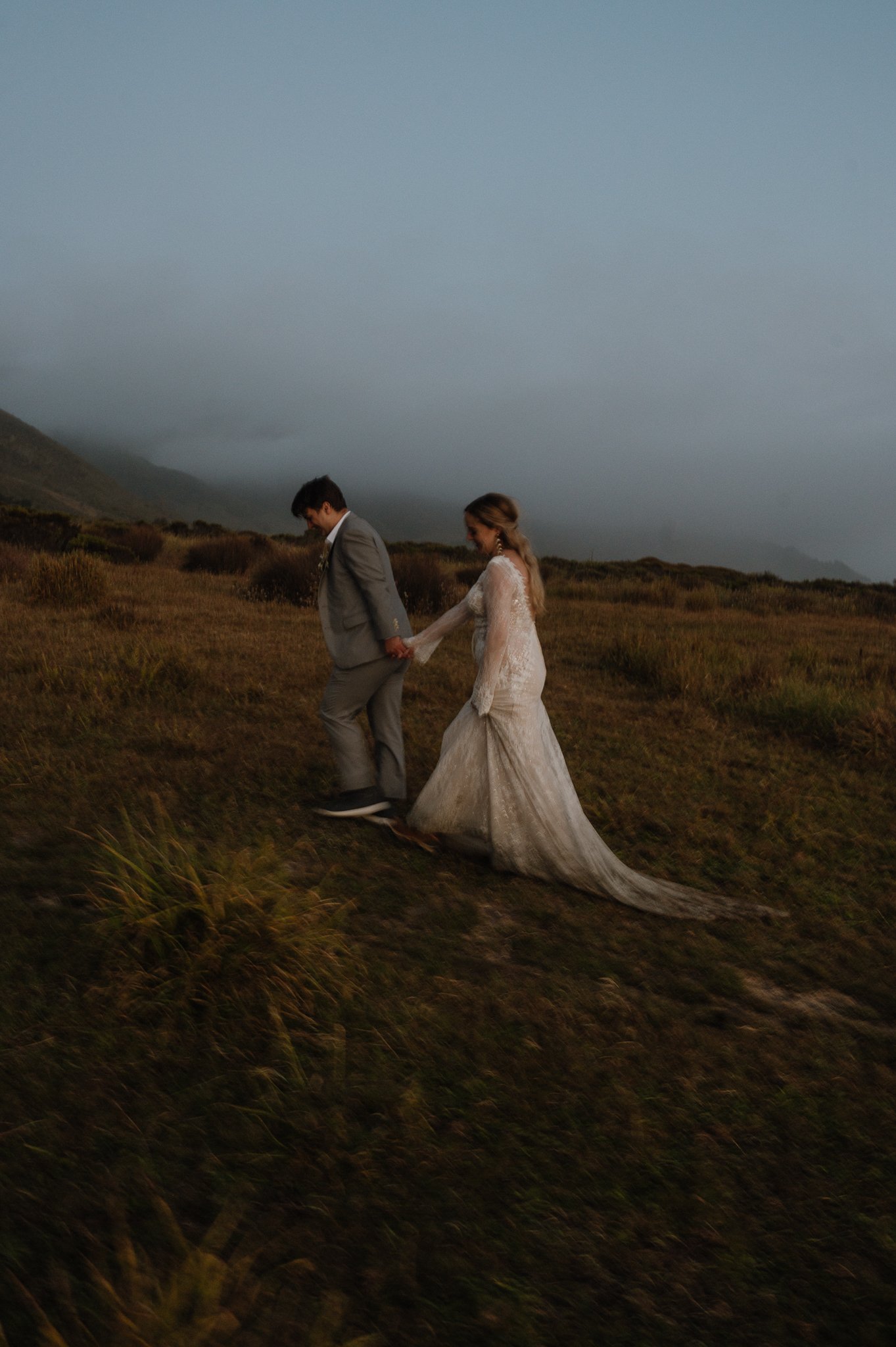 Big Sur Ventana wedding bride and groom walking holding hands up a hilly area through the grass