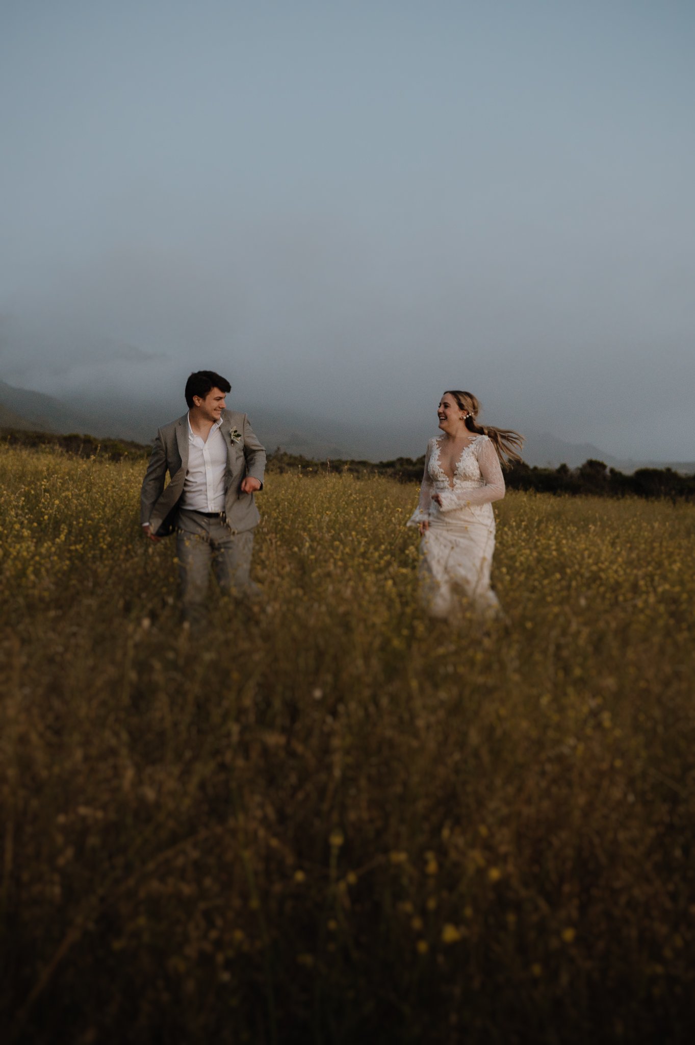 Big Sur Ventana wedding bride and groom running through grassy area smiling at each other
