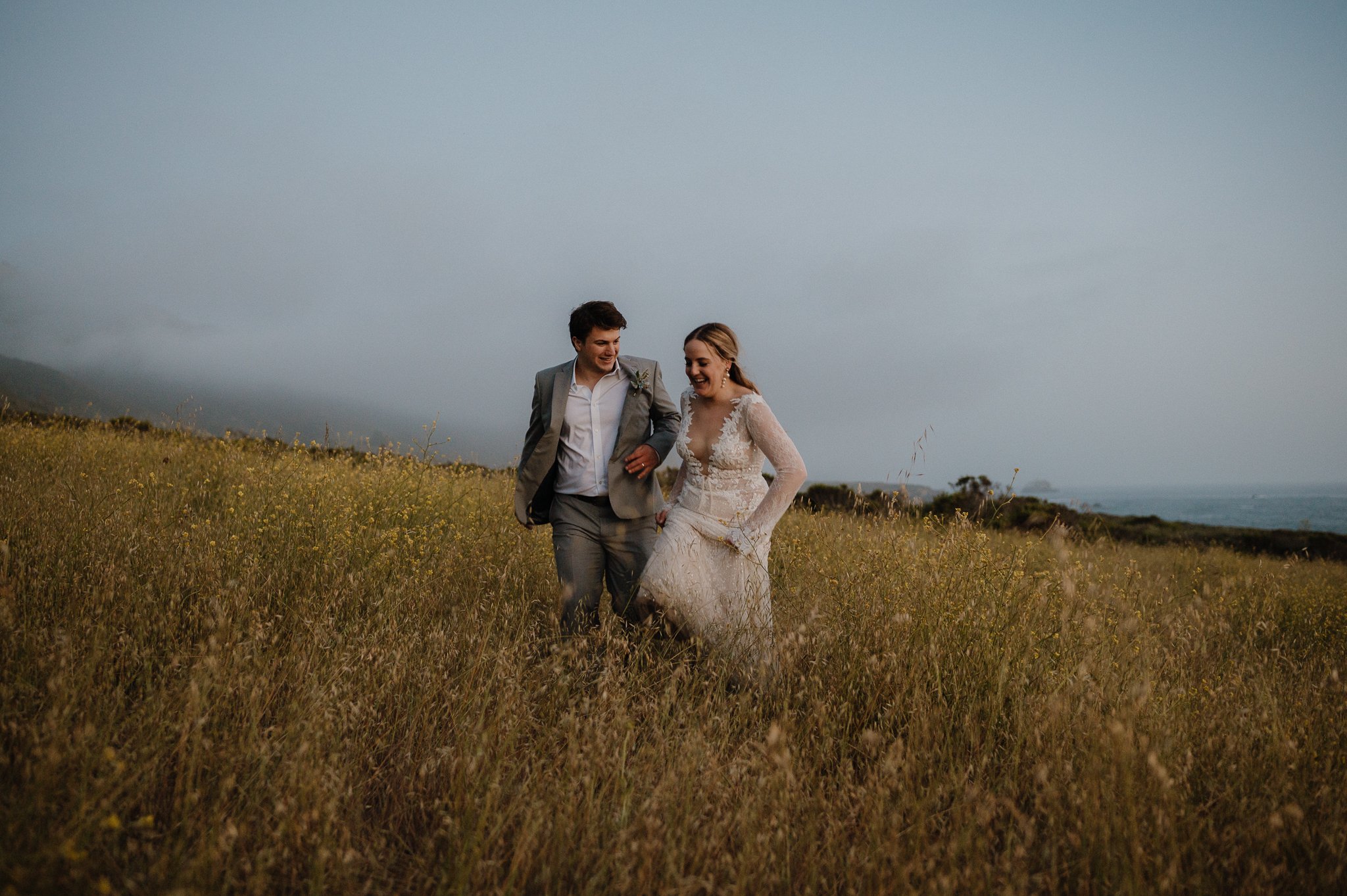 Big Sur Ventana wedding bride and groom running through grassy area smiling 