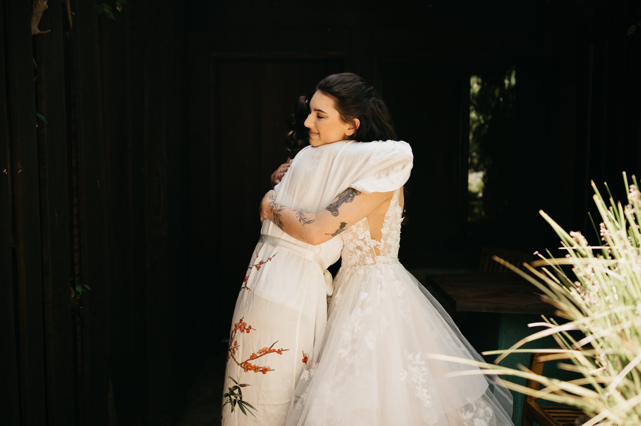 bride in wedding dress and maid of honor in robe hugging before ceremony Big Sur wedding