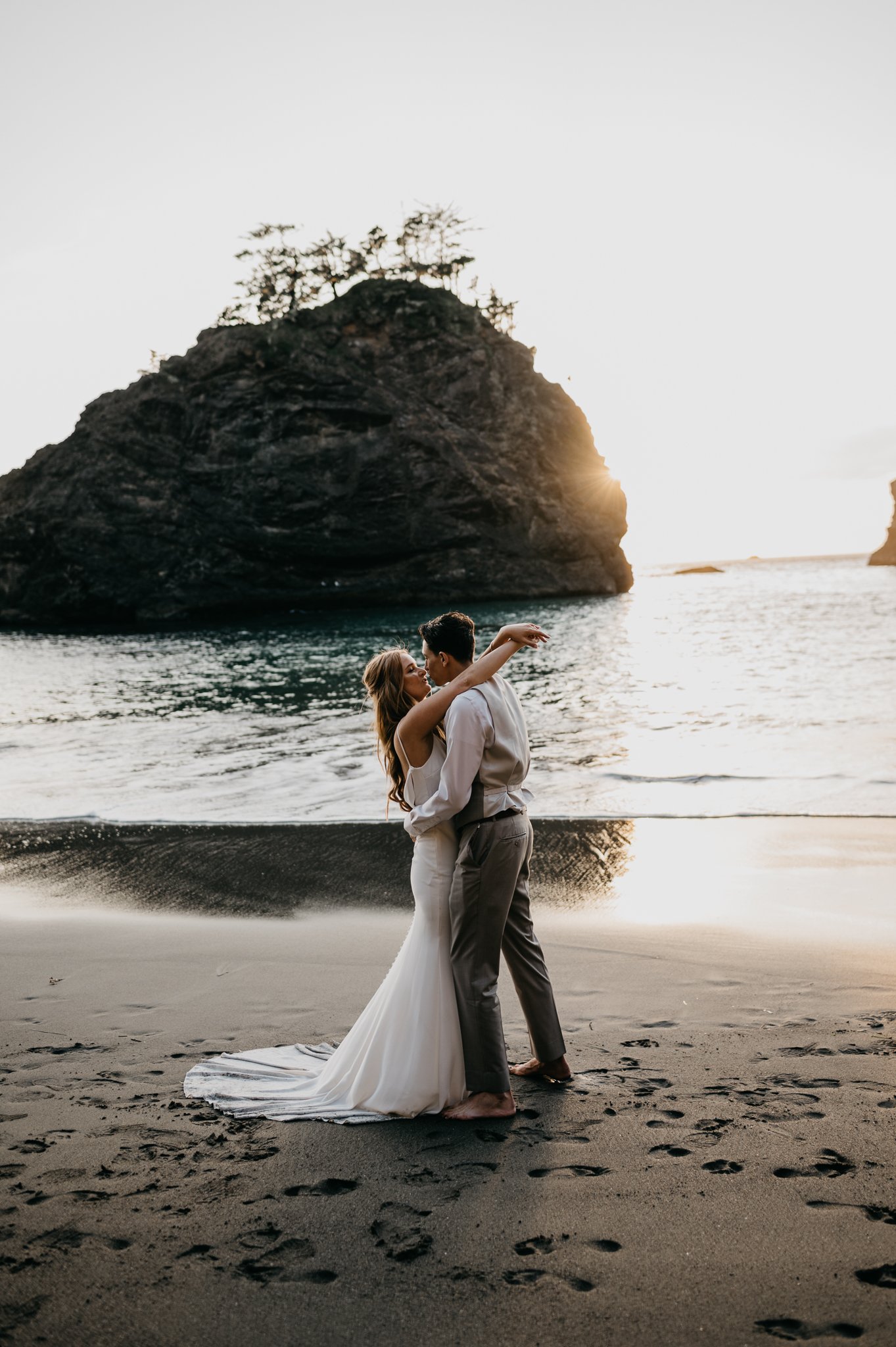Bride and groom in wedding attire kissing on beach at Samuel H. Boardman Beach in Oregon