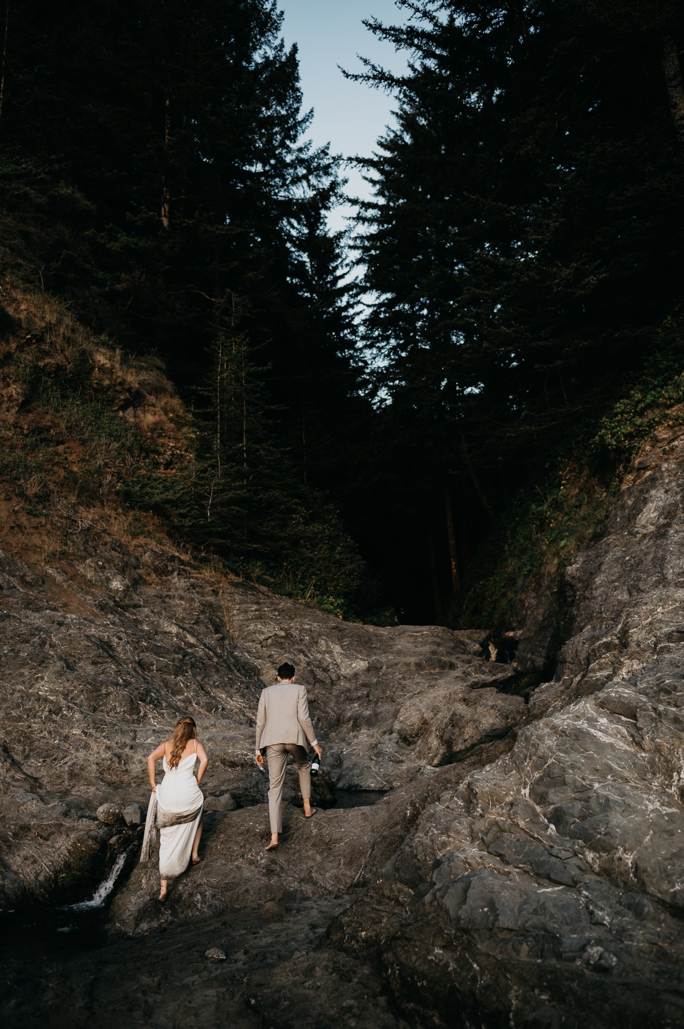Bride and groom in wedding attire hiking up coastal rocks along the Oregon Coast on their wedding day