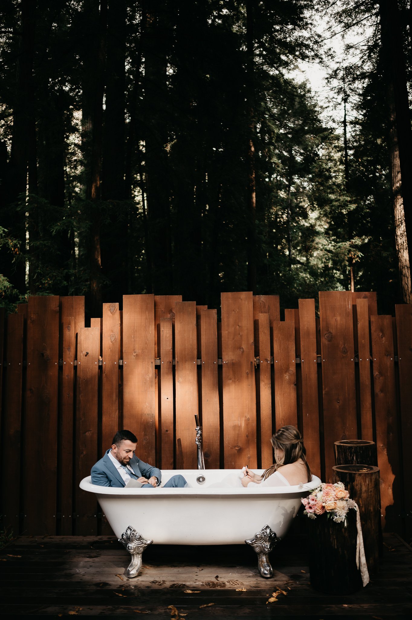 Bride and groom in Glen Oaks Big Sur sitting in a claw foot bathtub outside under the redwood trees writing their vows 