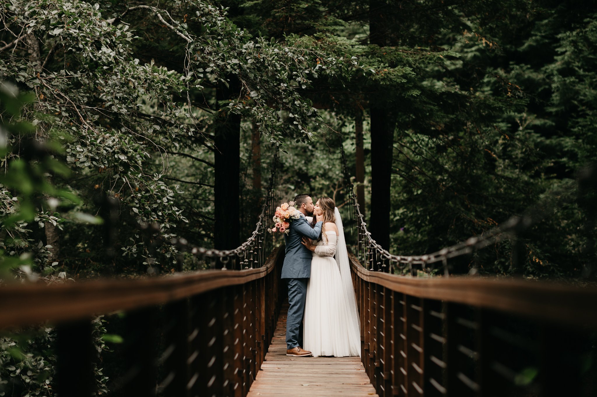 Bride and Groom in wedding attire standing on a Bridge holding hands before wedding ceremony tall redwoods in background