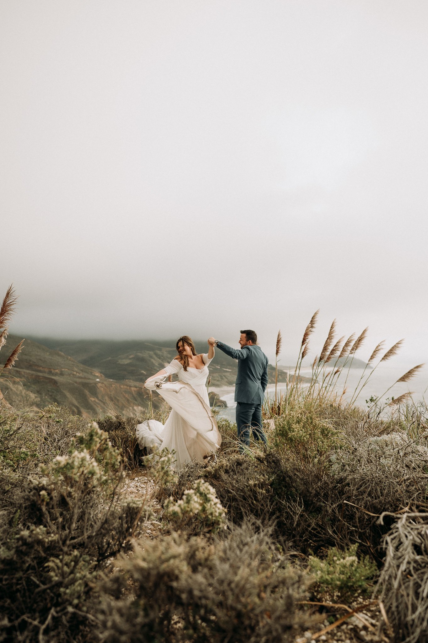 Bride and groom after wedding ceremony dancing on a cliff overlooking the Pacific Ocean in Big Sur