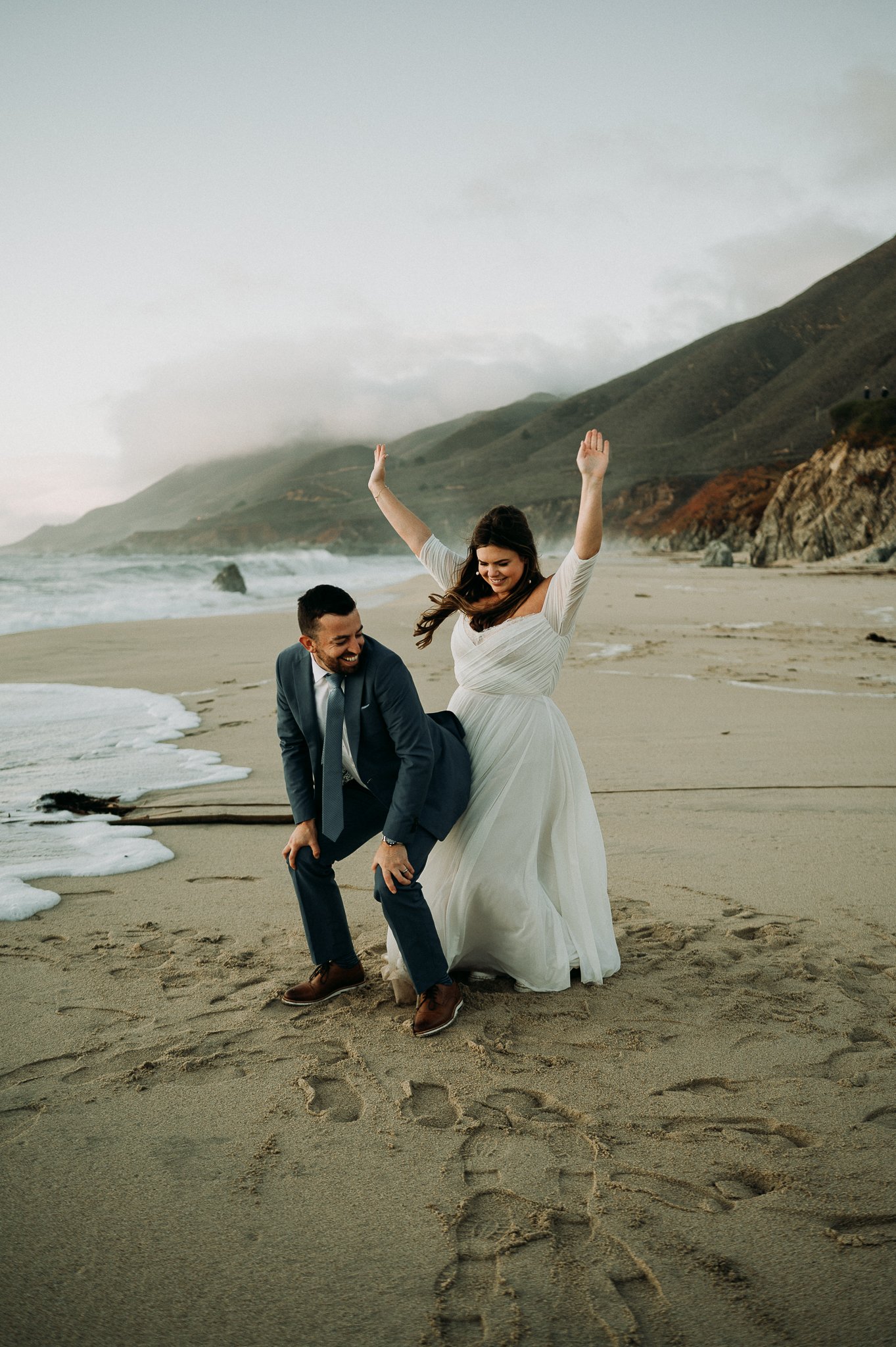 Bride and Groom in wedding attire dancing in the Beach in Big Sur, California